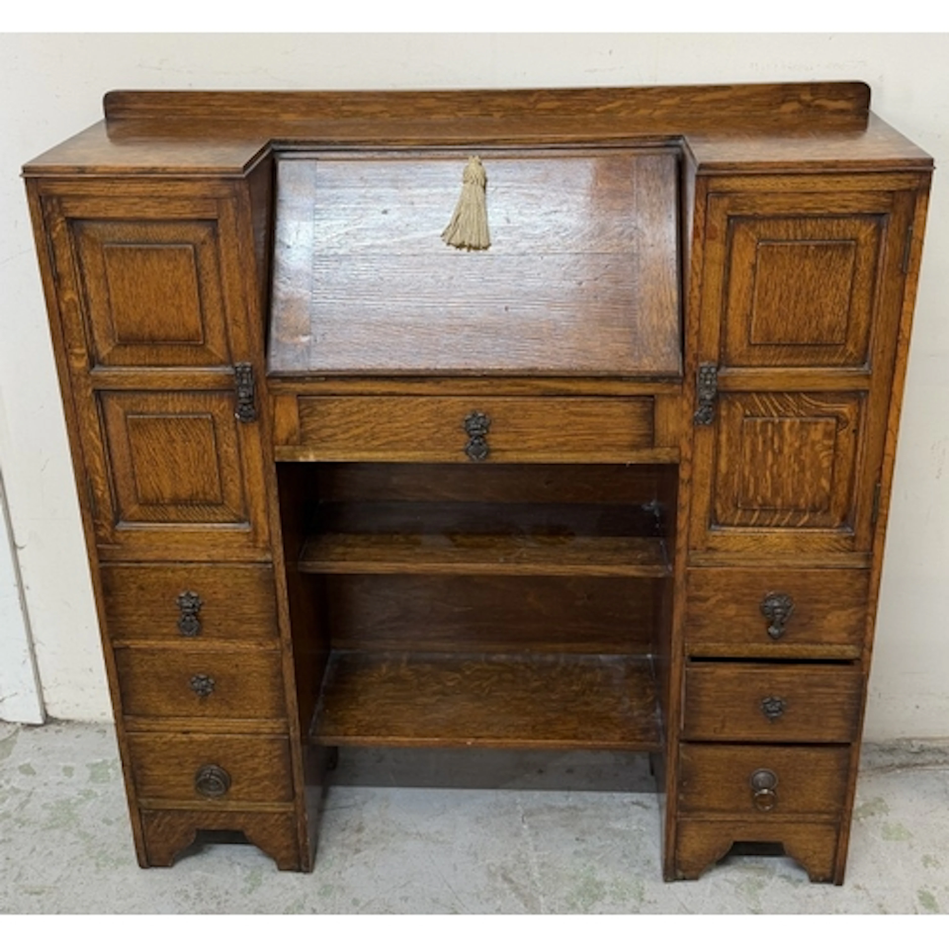 An oak bureau with hinged writing table flanked by cupboards...
