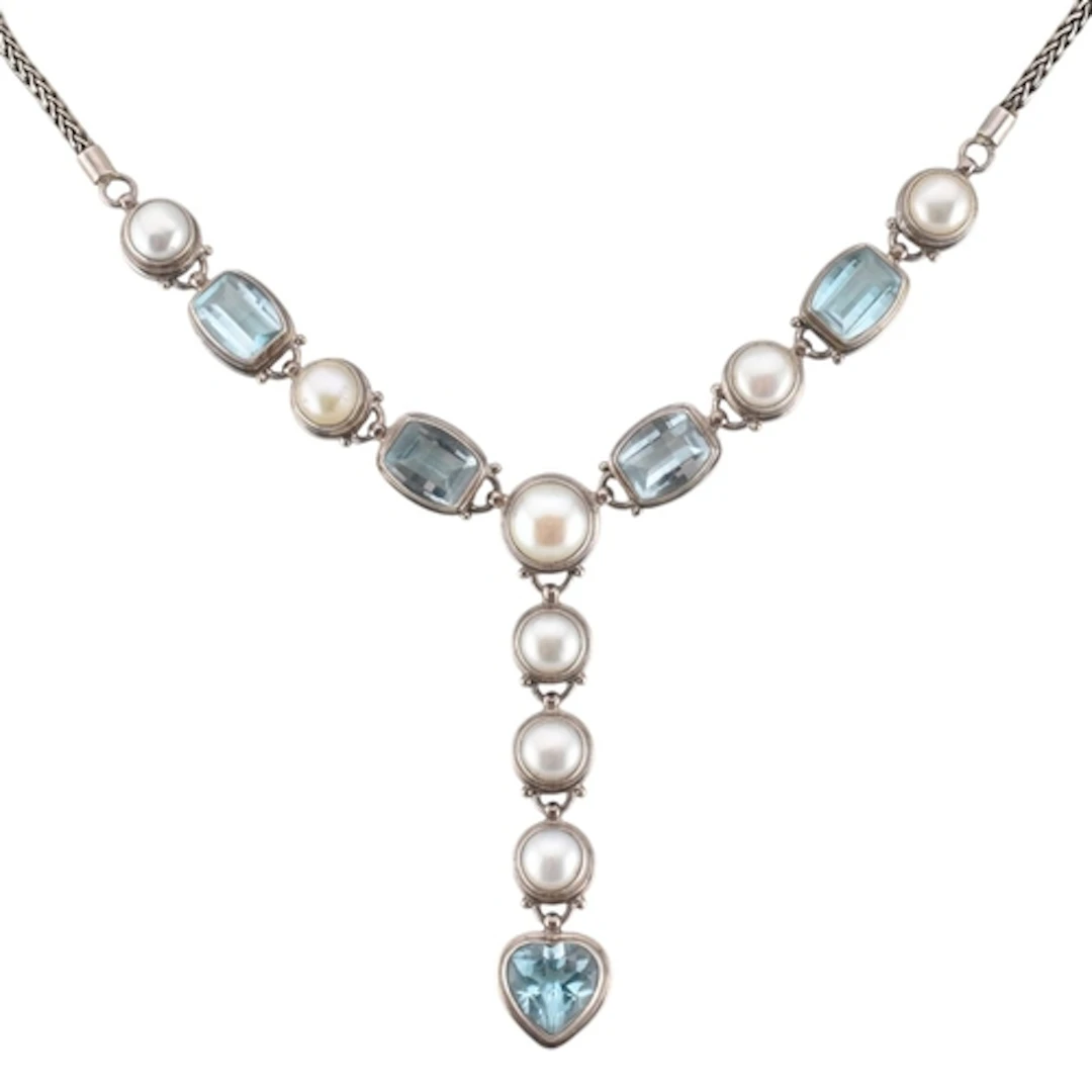A silver pearl and blue topaz heart drop necklace. A silver ...