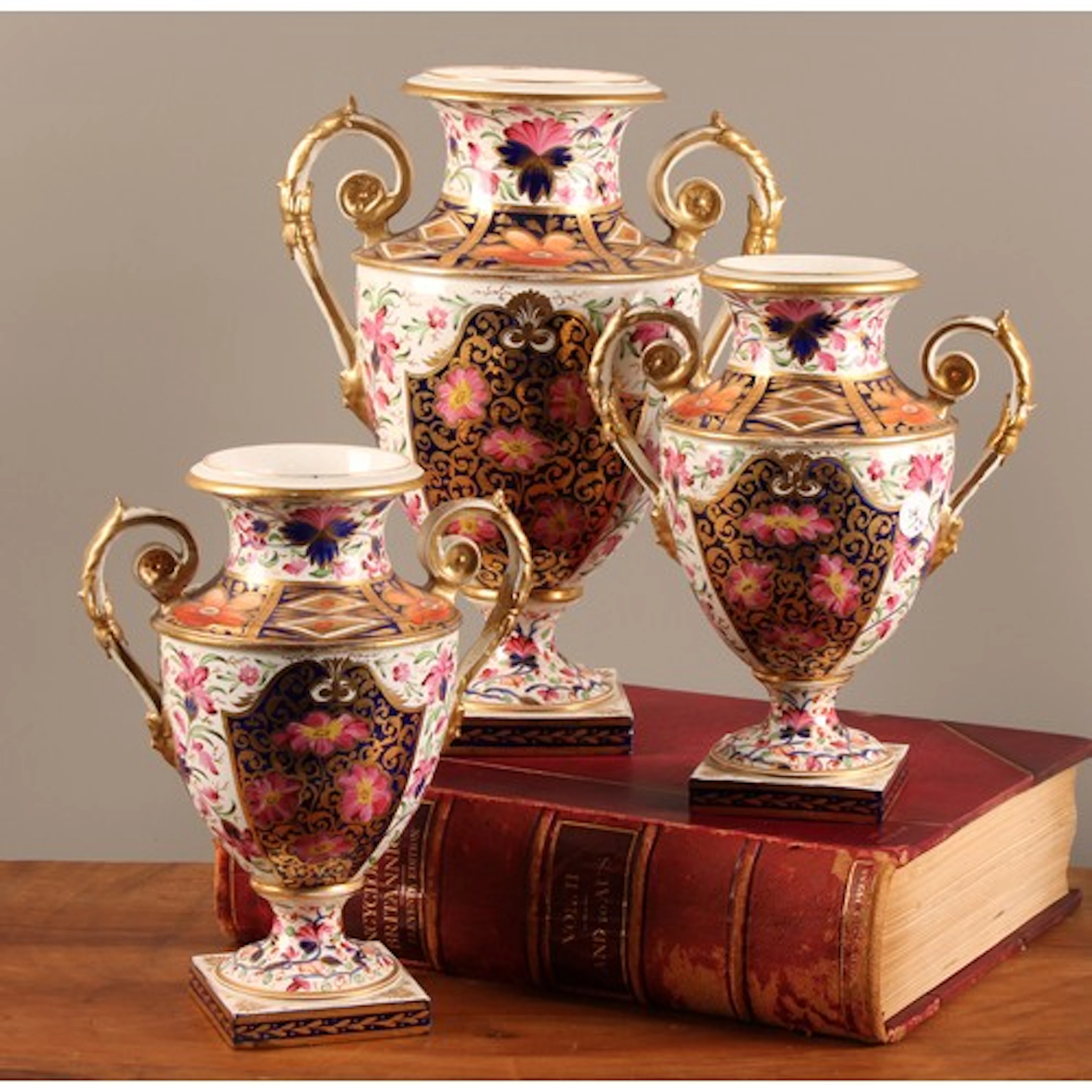 A garniture of three Bloor Derby ovoid pedestal urns, painte...
