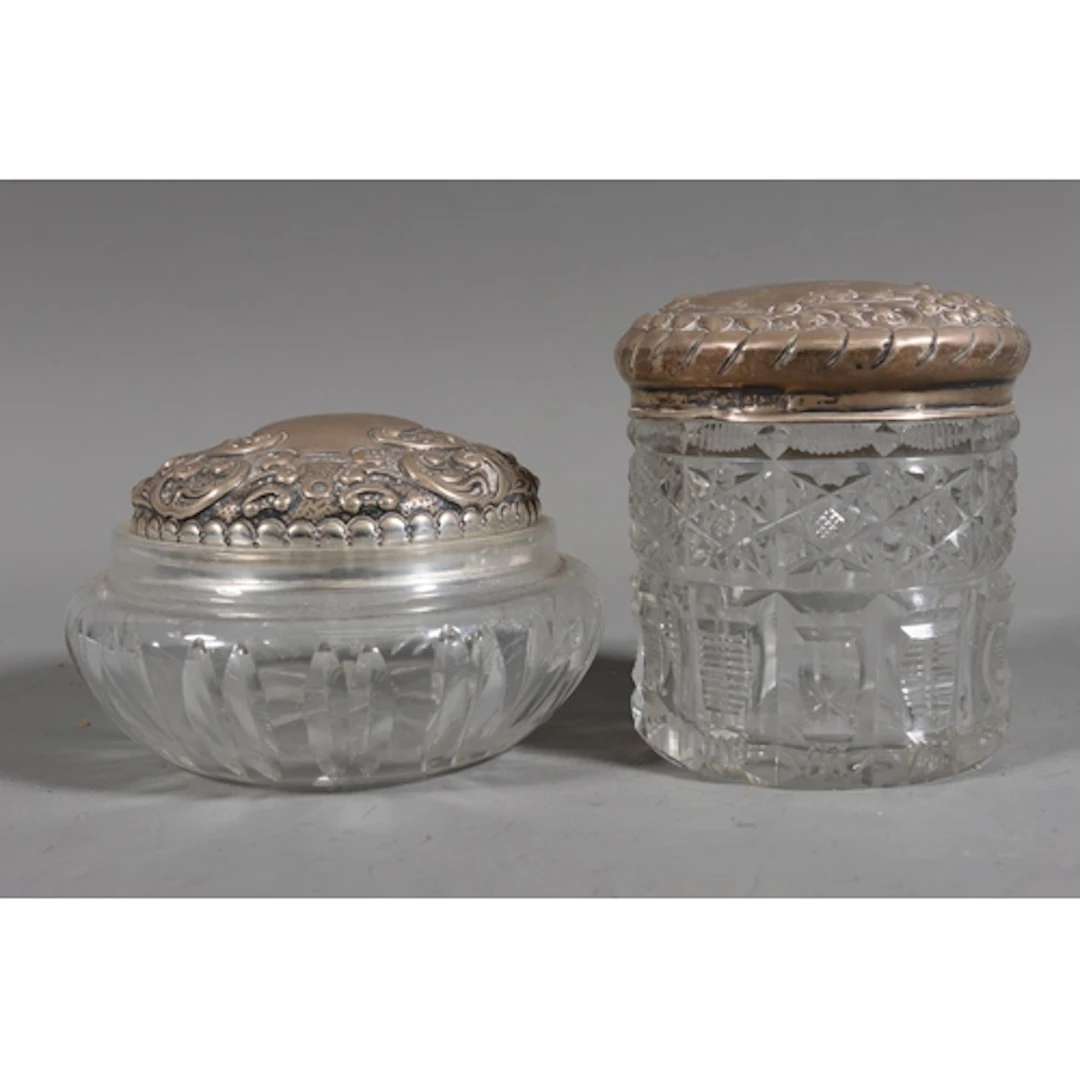 Two cut glass toilet jars with silver covers, the silver lid...