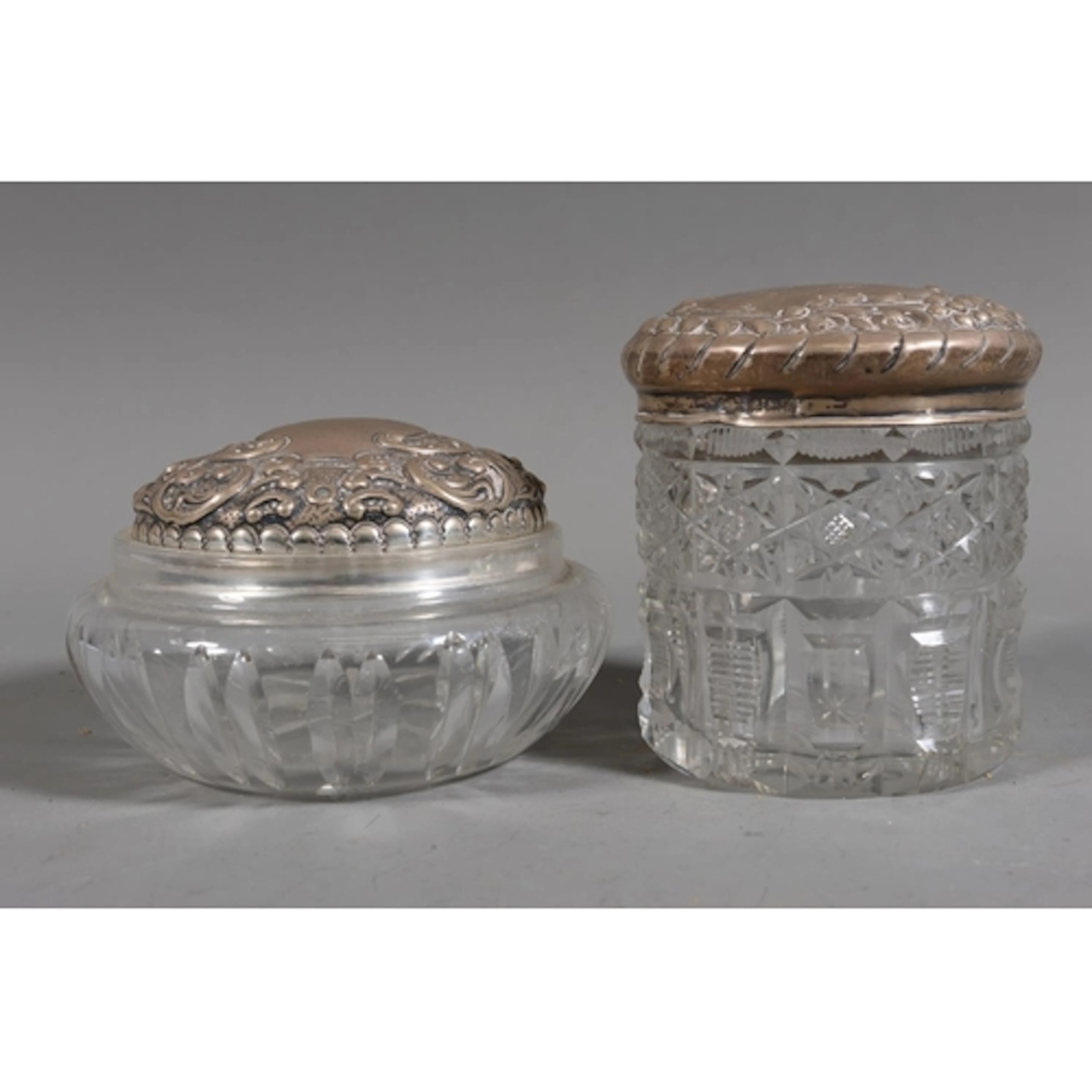 Two cut glass toilet jars with silver covers, the silver lid...