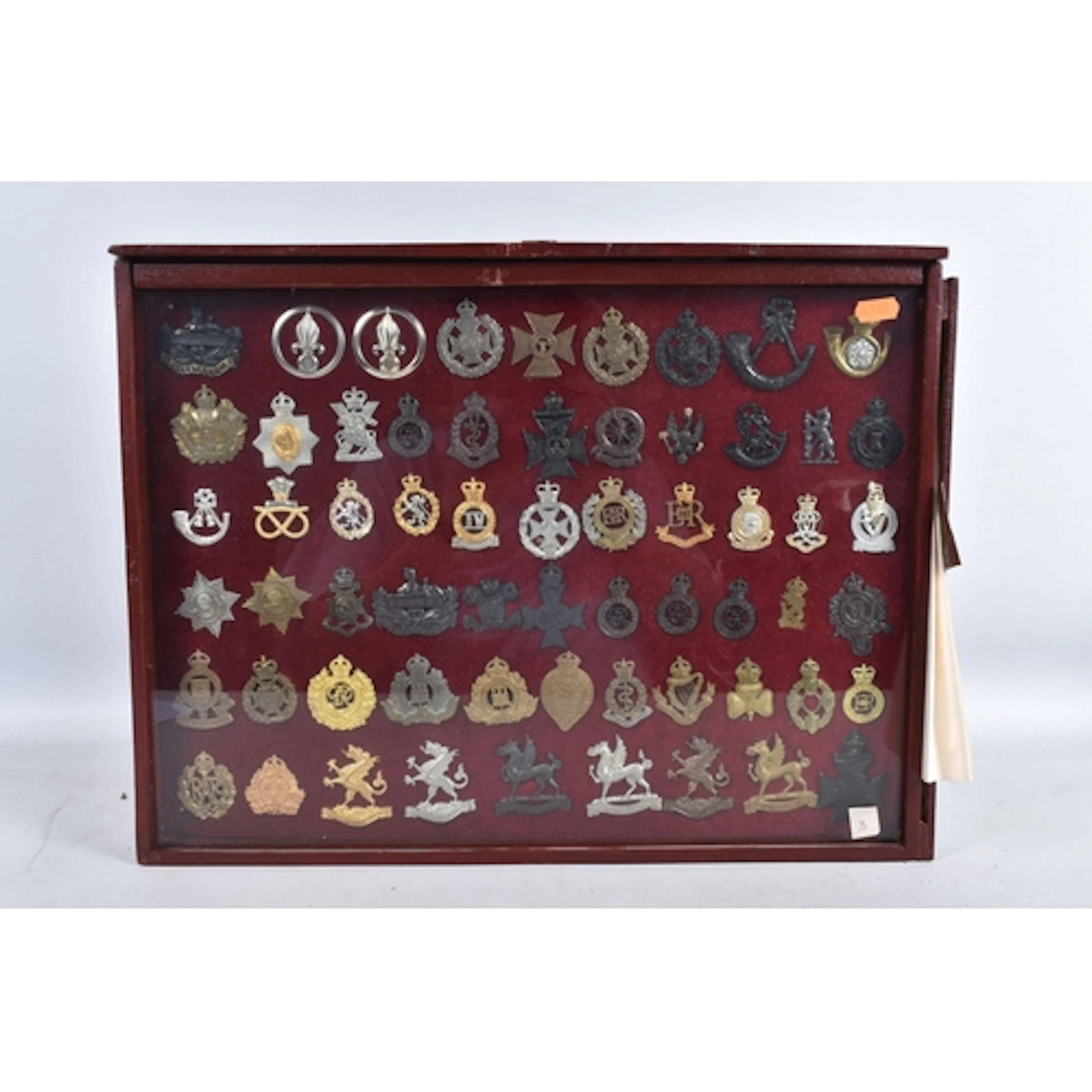 A GLAZED DISPLAY CASE CONTAINING A COLLECTION OF MILITARY BA...