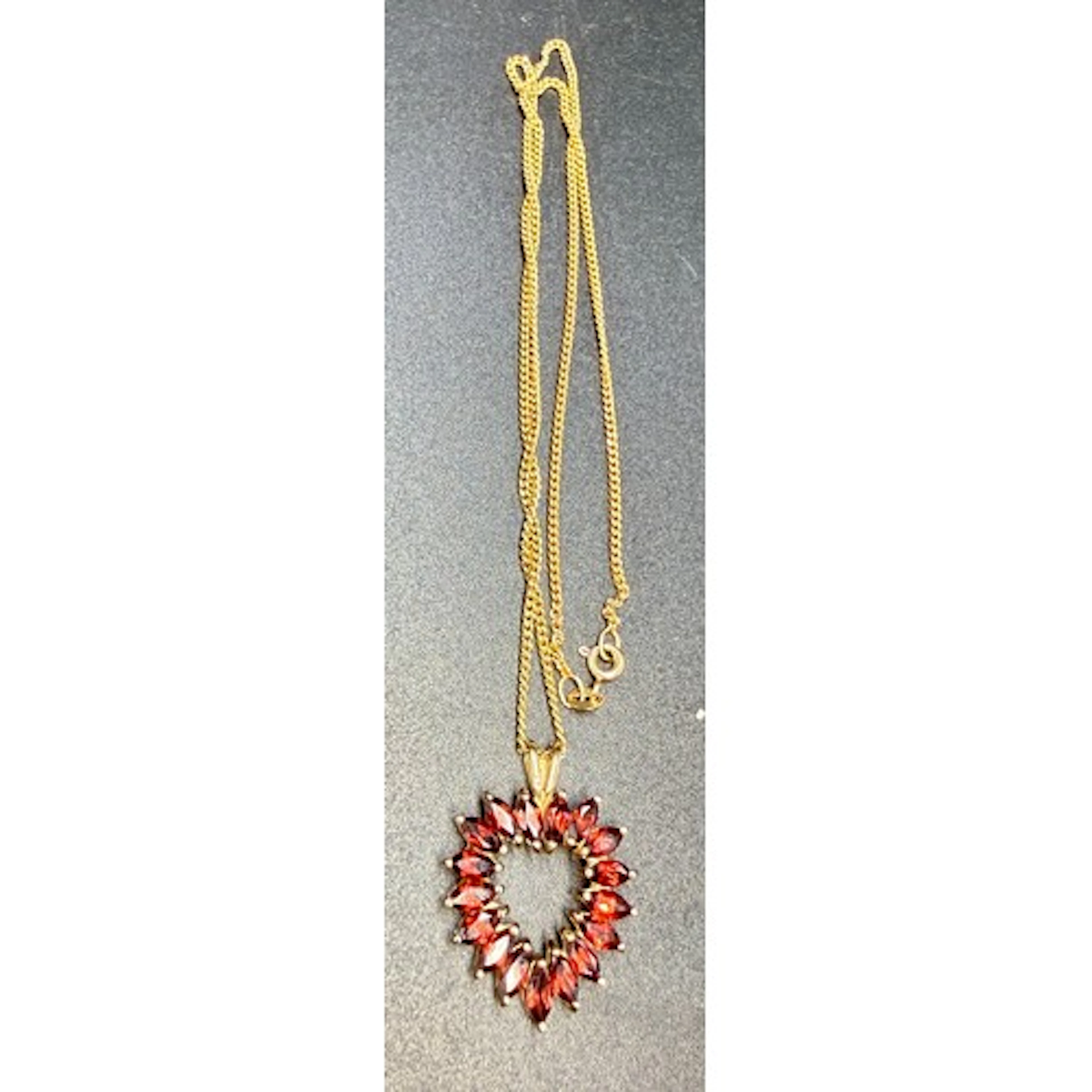 A 9 carat gold heart shaped pendant set with garnets suspend...