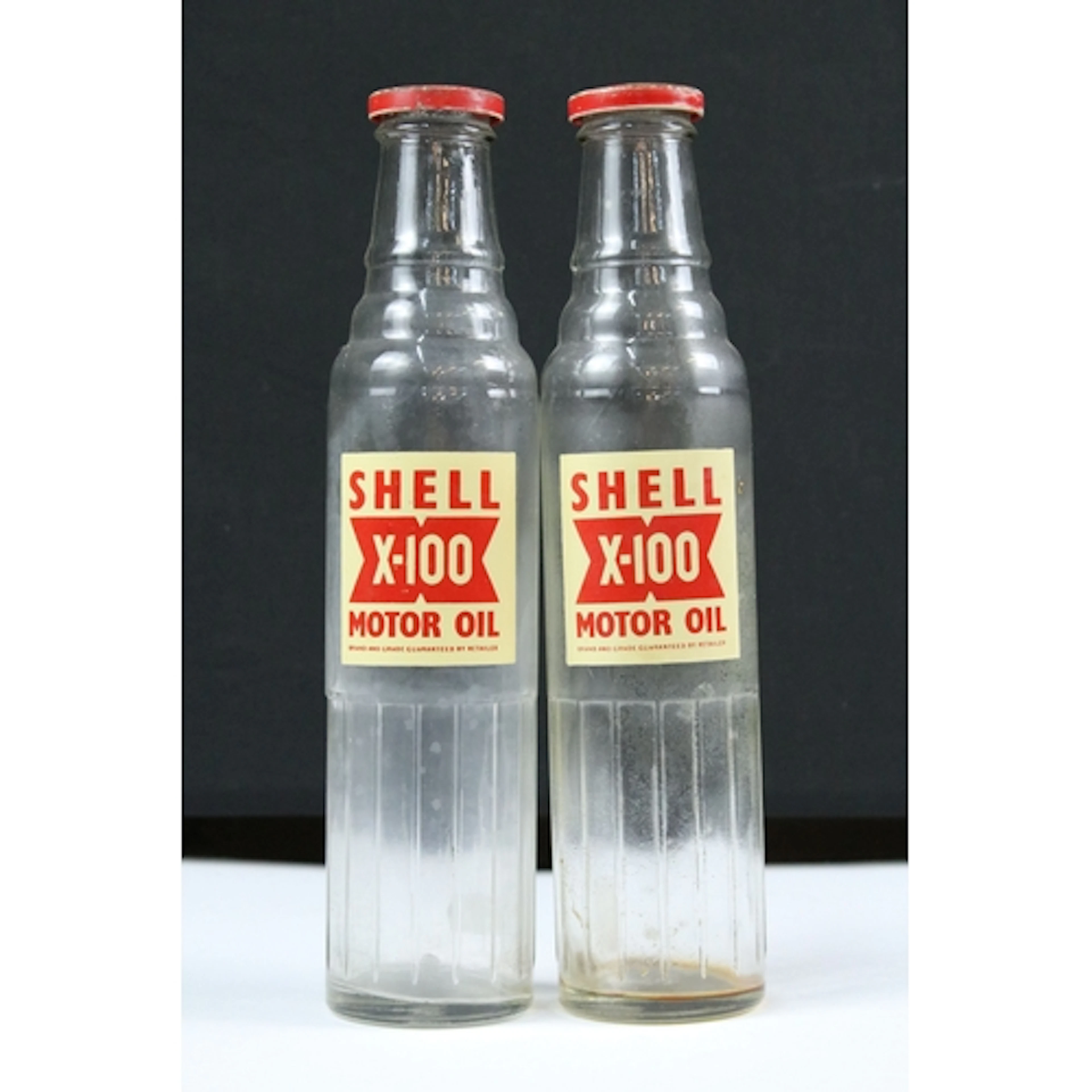 Two Shell X-100 Motor Oil glass bottles, the lids marked '20...