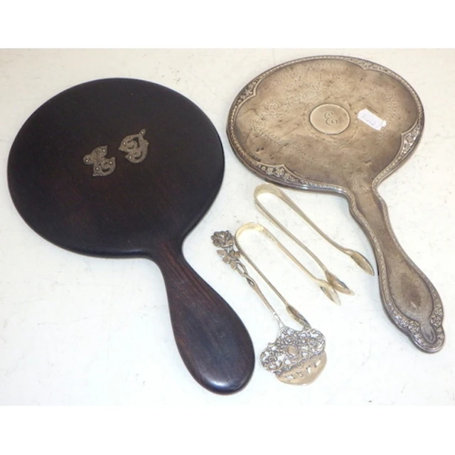 A silver vanity mirror, ebony mirror, two silver sugar tongs...