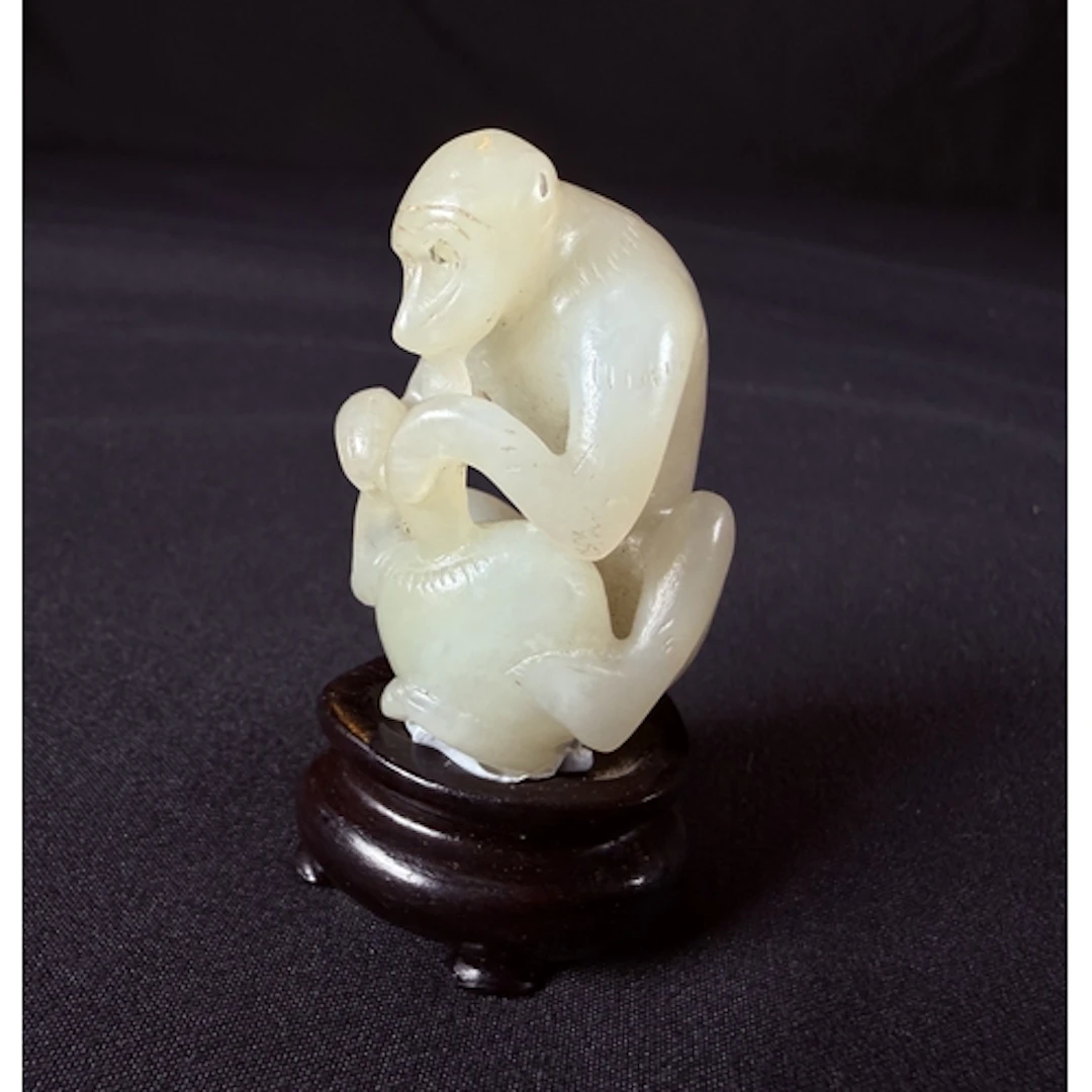 A Chinese pale green jade carved figure of a seated monkey h...