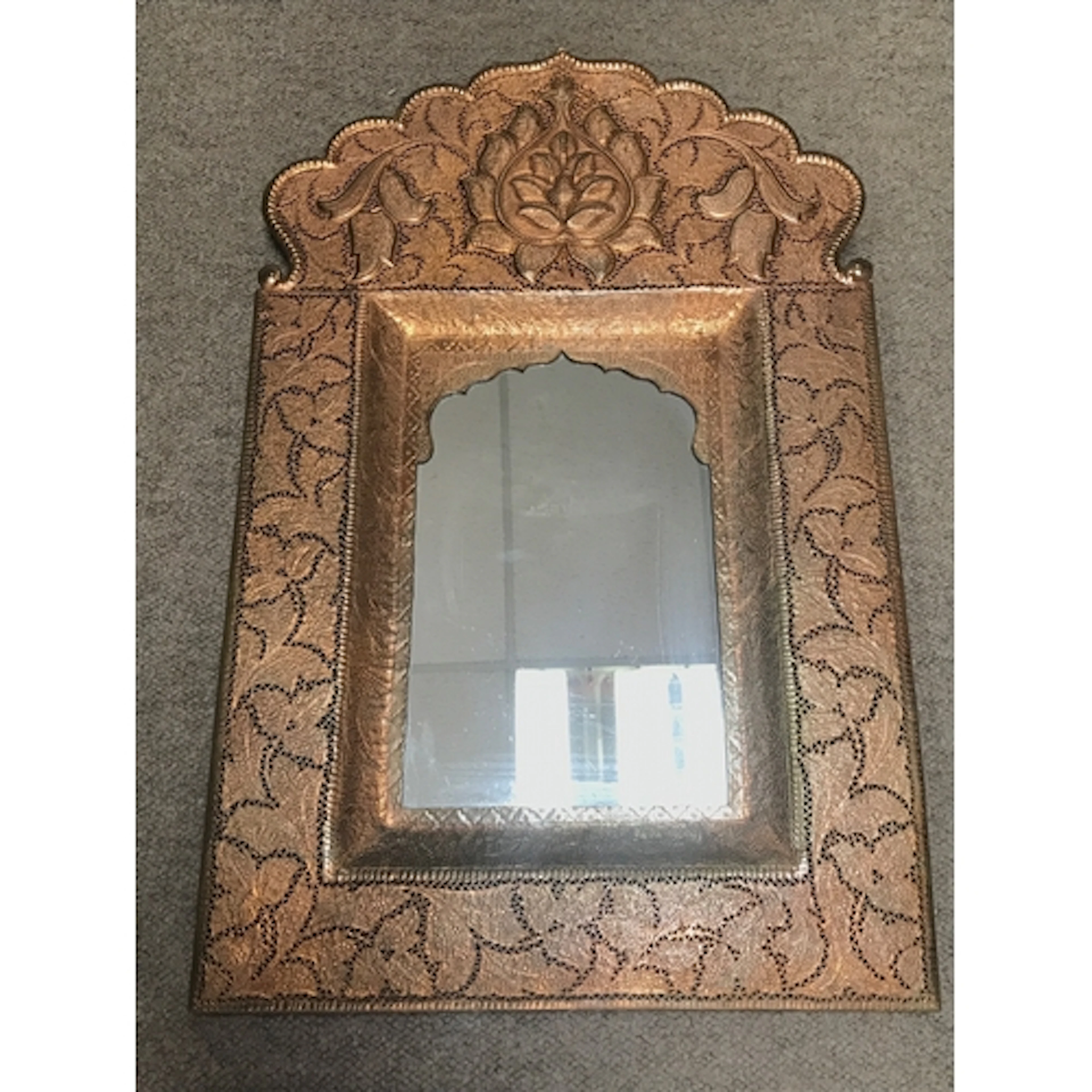 An antique copper wall mirror features elaborate hammered an...