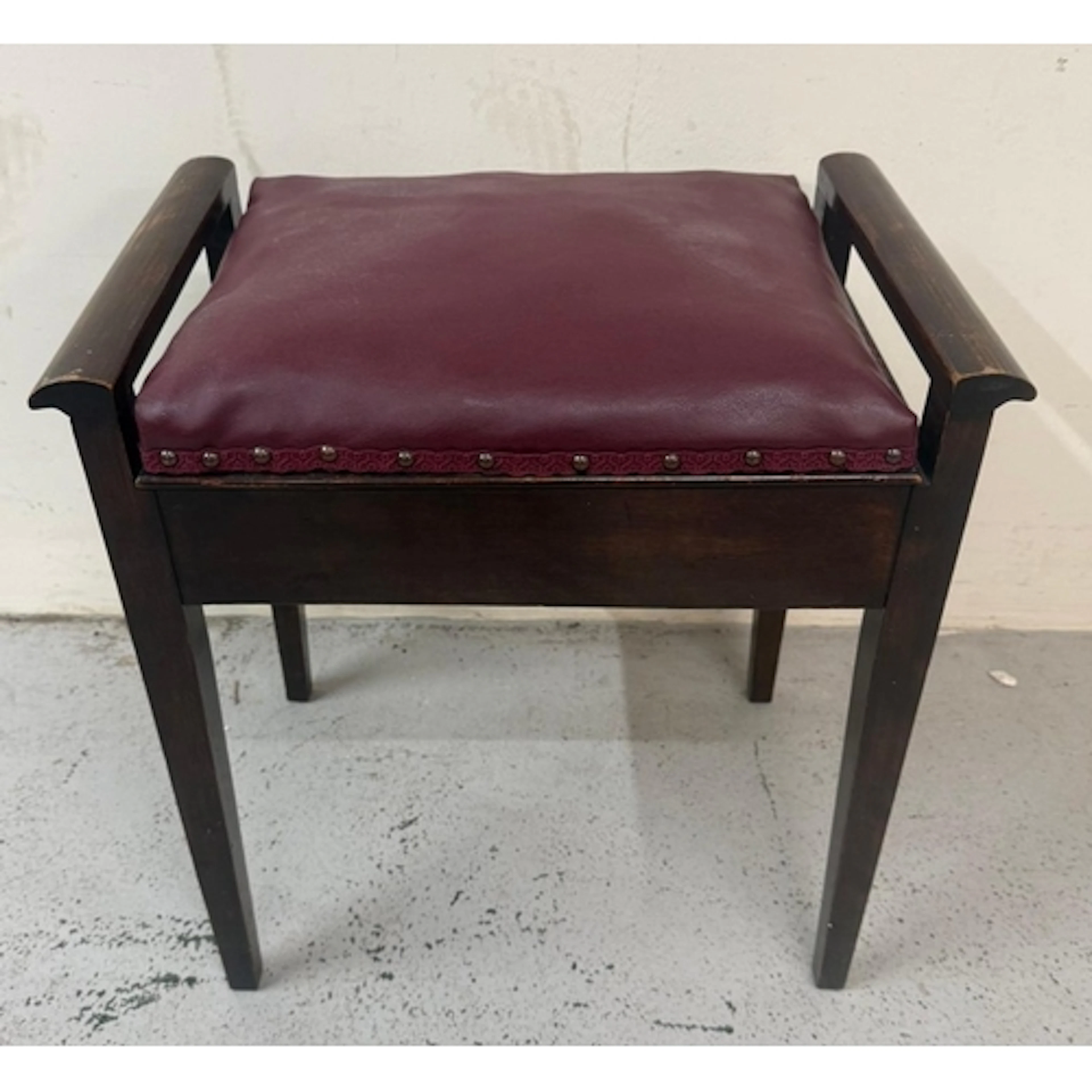 A mahogany-framed piano stool with a red leather seat