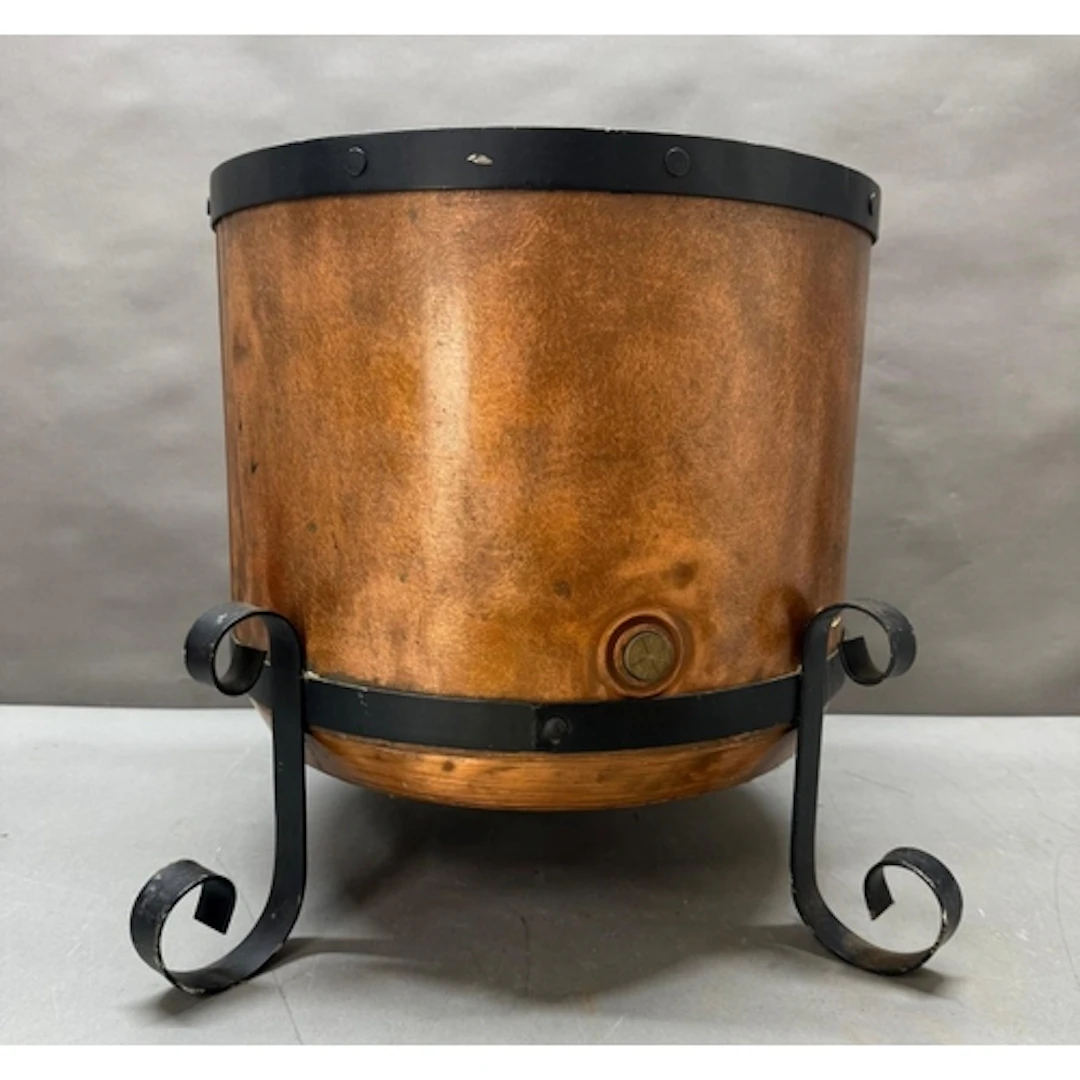 A large copper water boiler converted to a log bin on a forg...