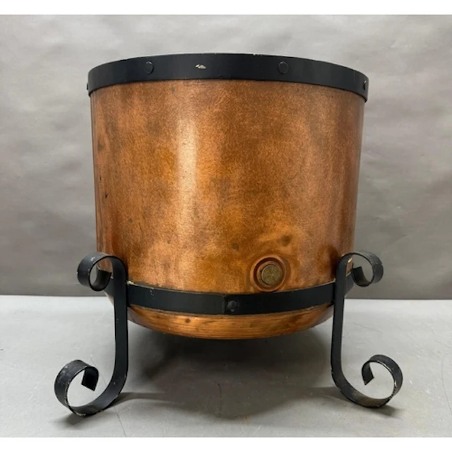 A large copper water boiler converted to a log bin on a forg...