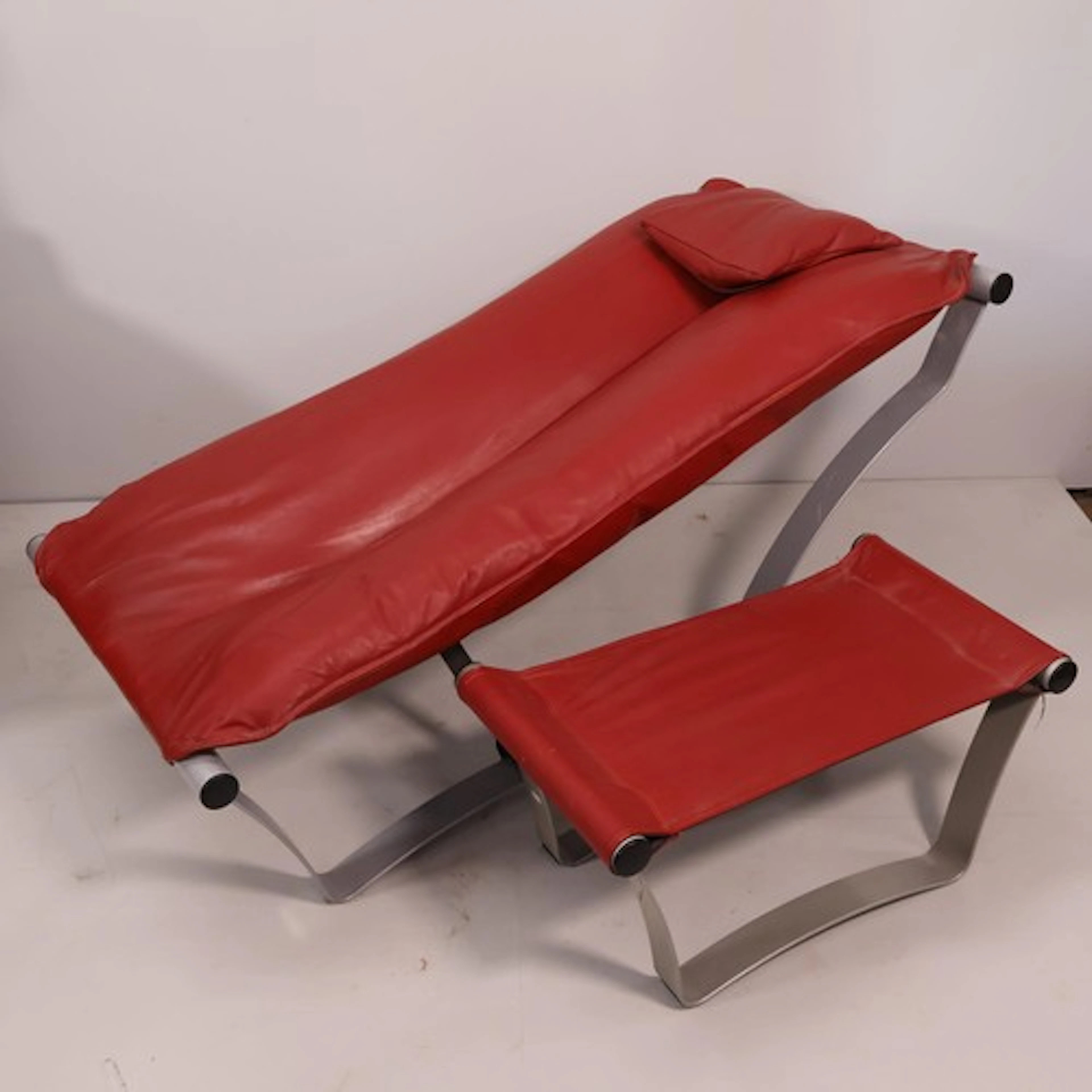 A modern red faux-leather upholstered lounge chair with slin...