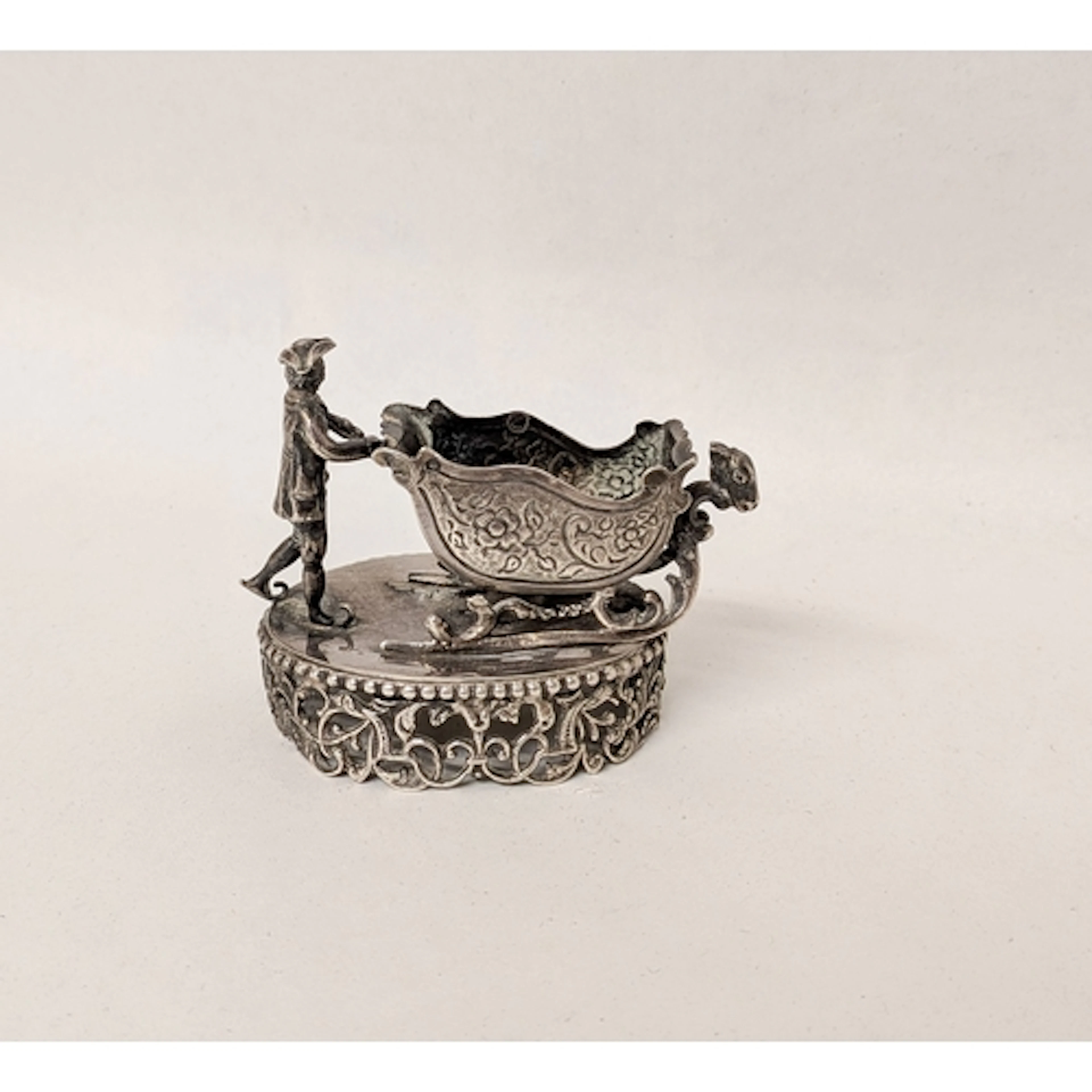 A continental silver toy modelled as a man pushing a sleigh,...