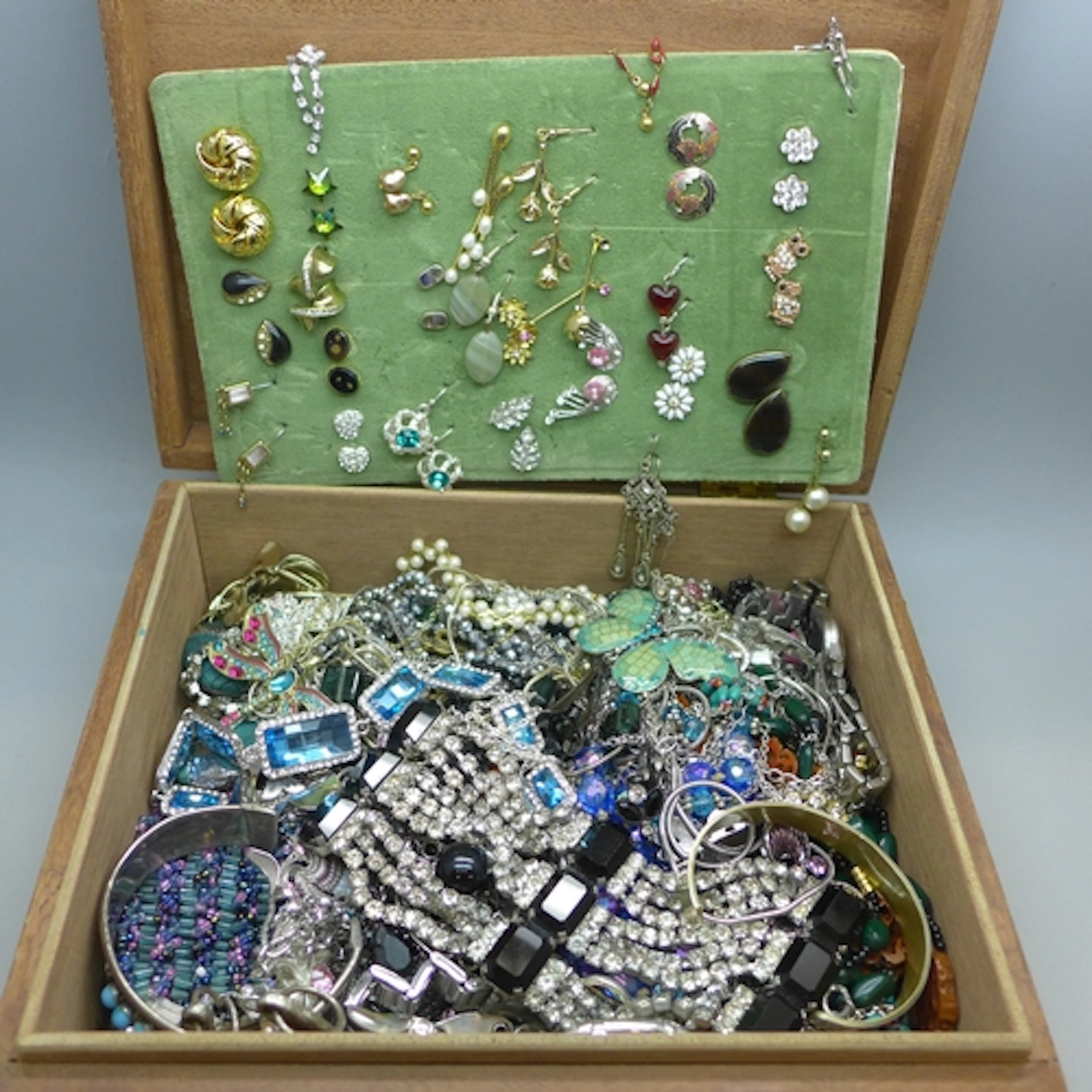 A wooden box of costume jewellery including bangles, necklac...