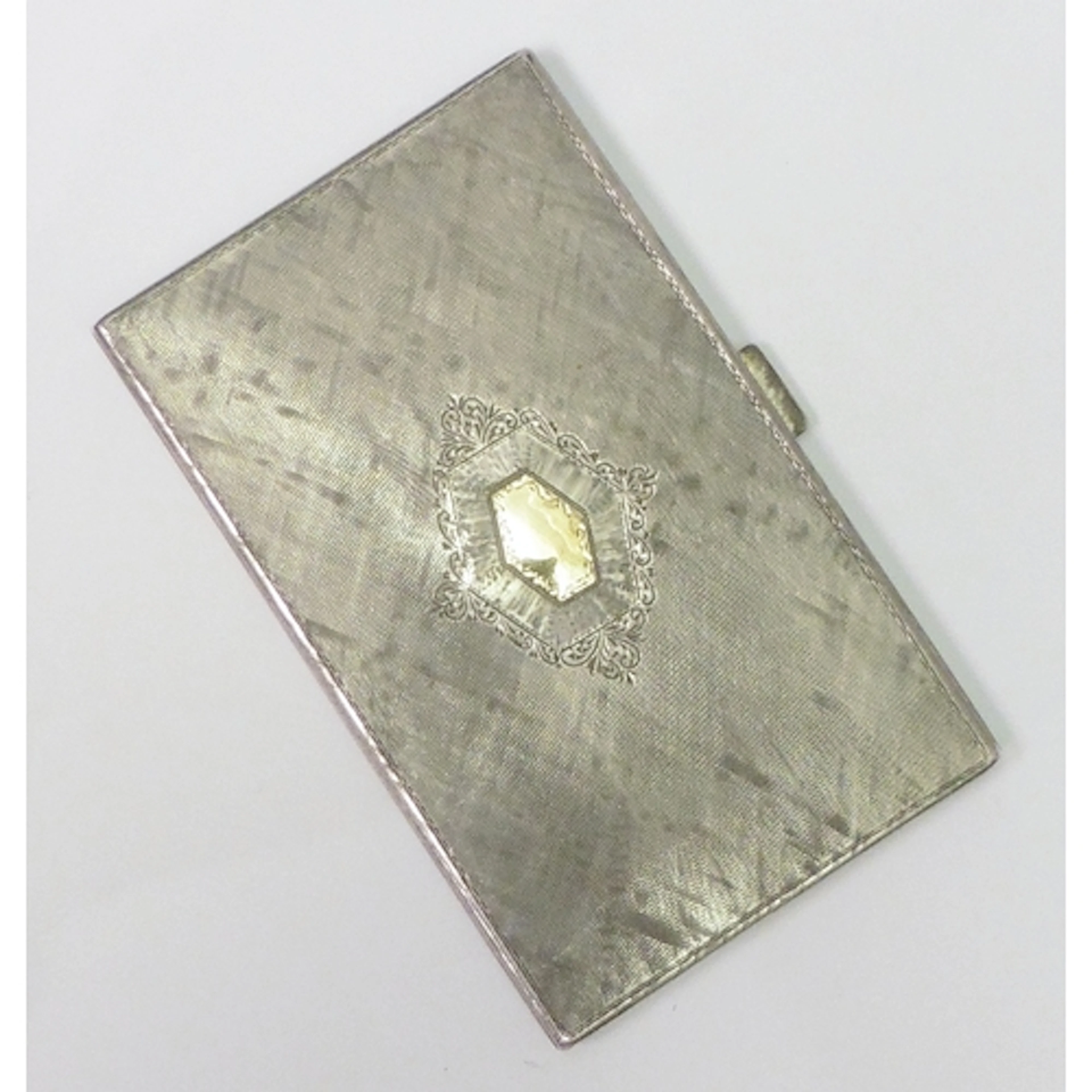 A cigarette case, engine turned white metal with a yellow me...