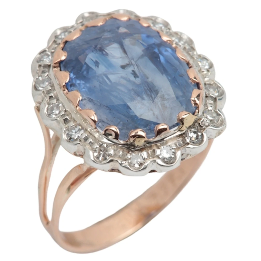 A sapphire and diamond cluster ring, claw-set with an oval s...