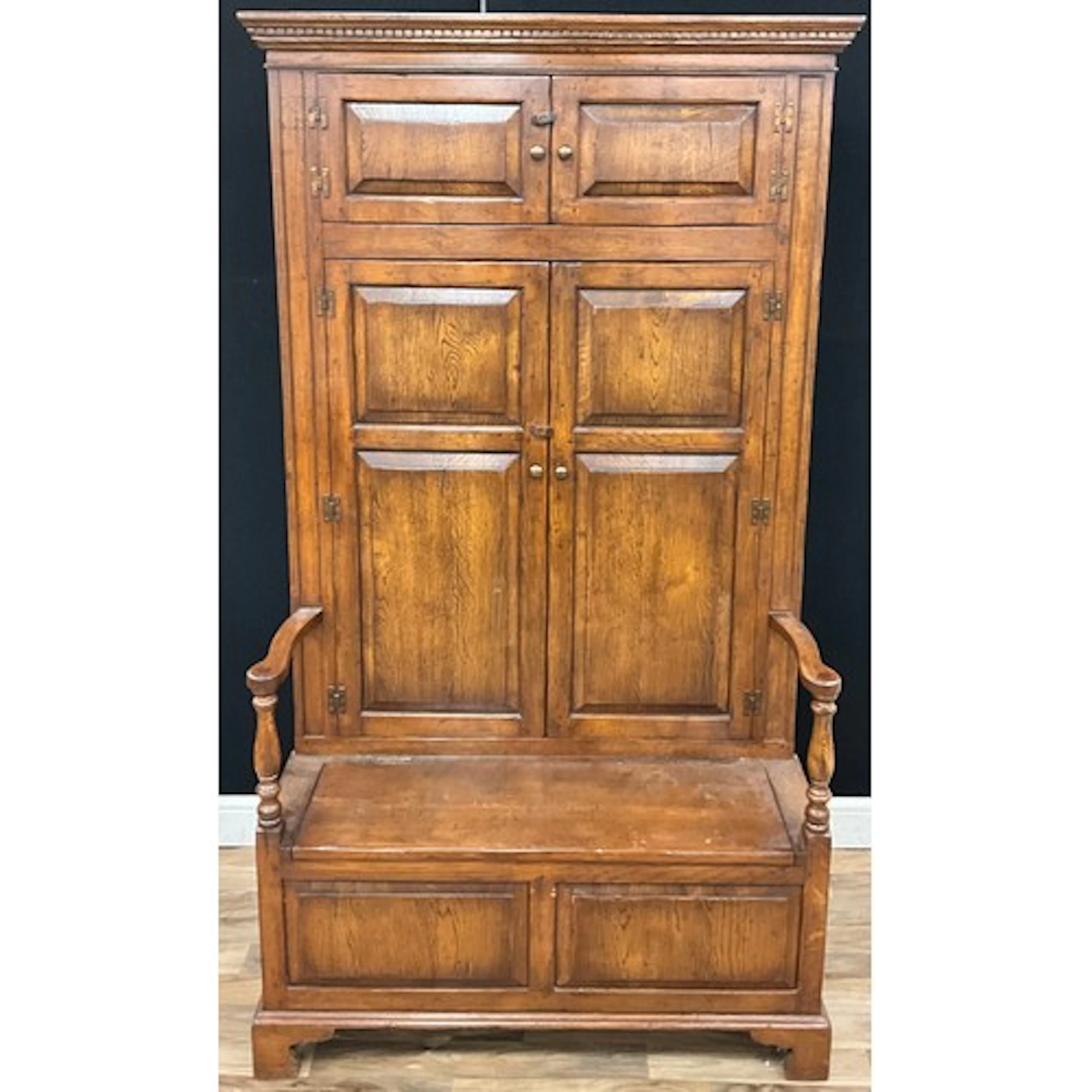 A George III style oak bacon settle, panel doors, hinged sea...