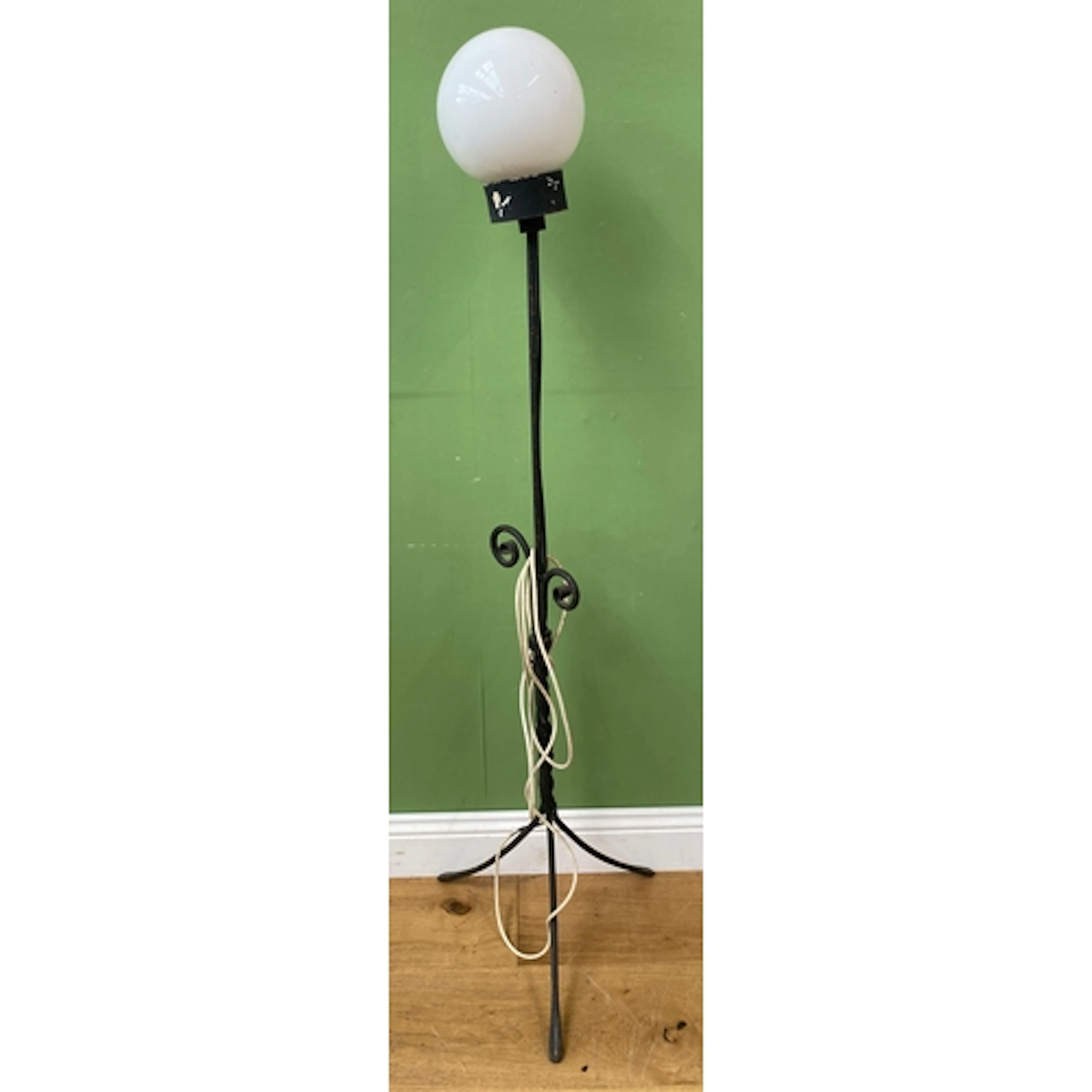 A wrought metal standard lamp with milk glass orb shade
