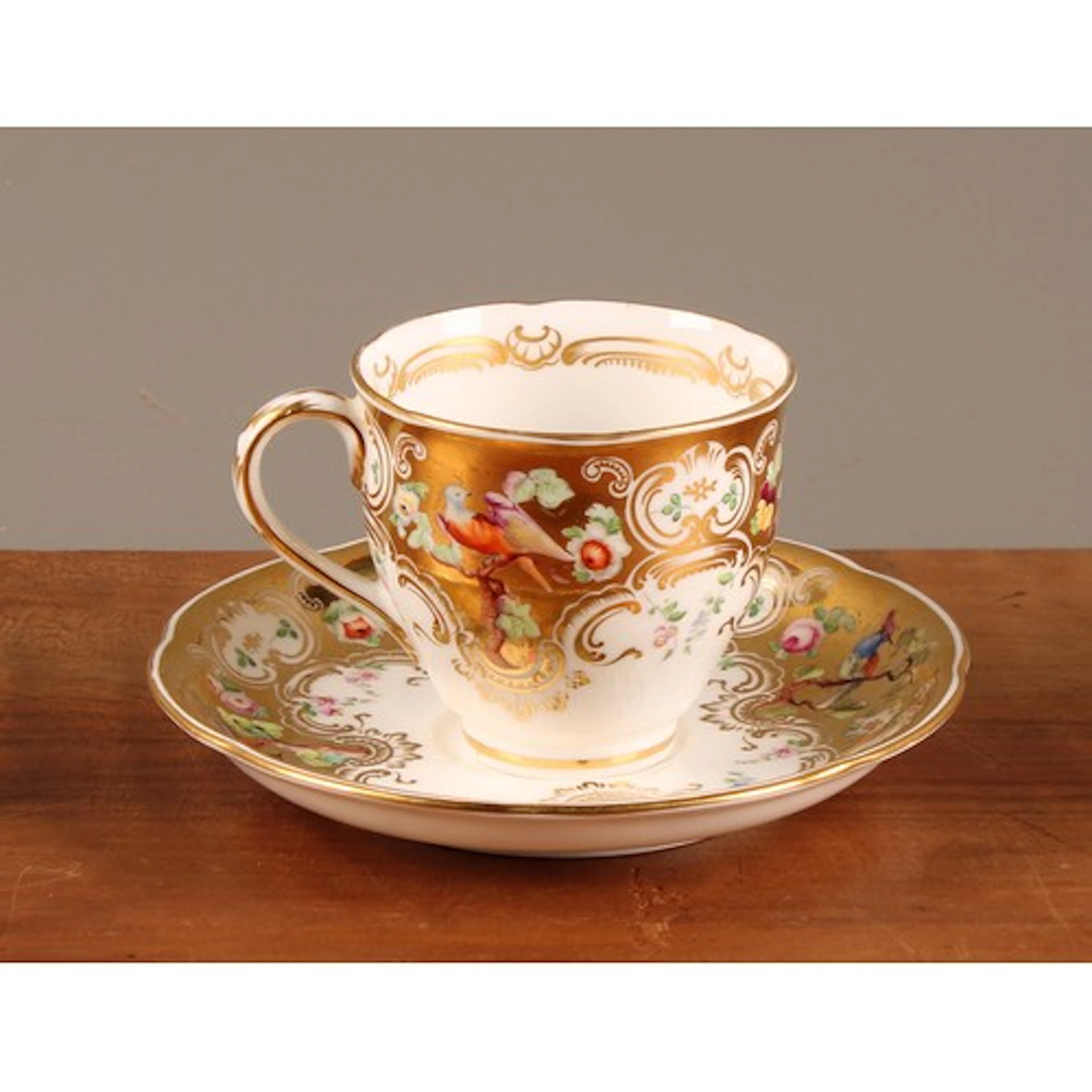 A Coalport teacup and saucer, painted with flowers and birds...