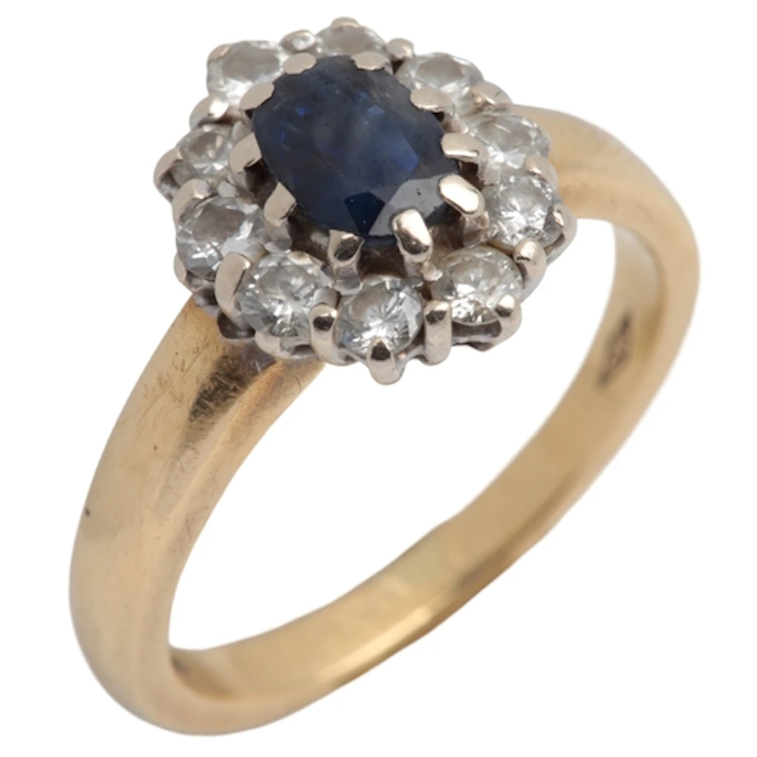 A sapphire and diamond cluster ring, claw-set with an oval s...