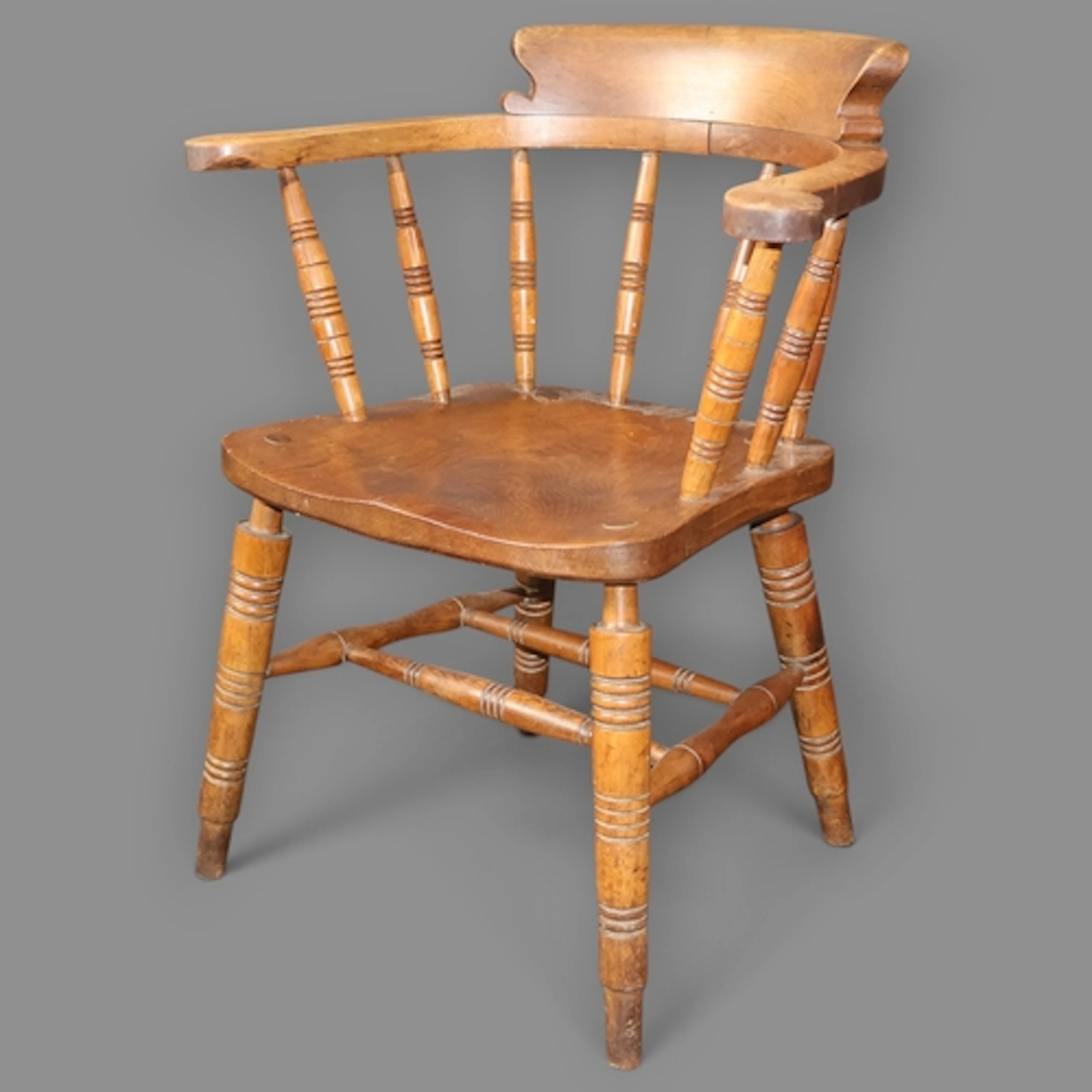 An antique elm-seated smoker's bow arm desk chair.