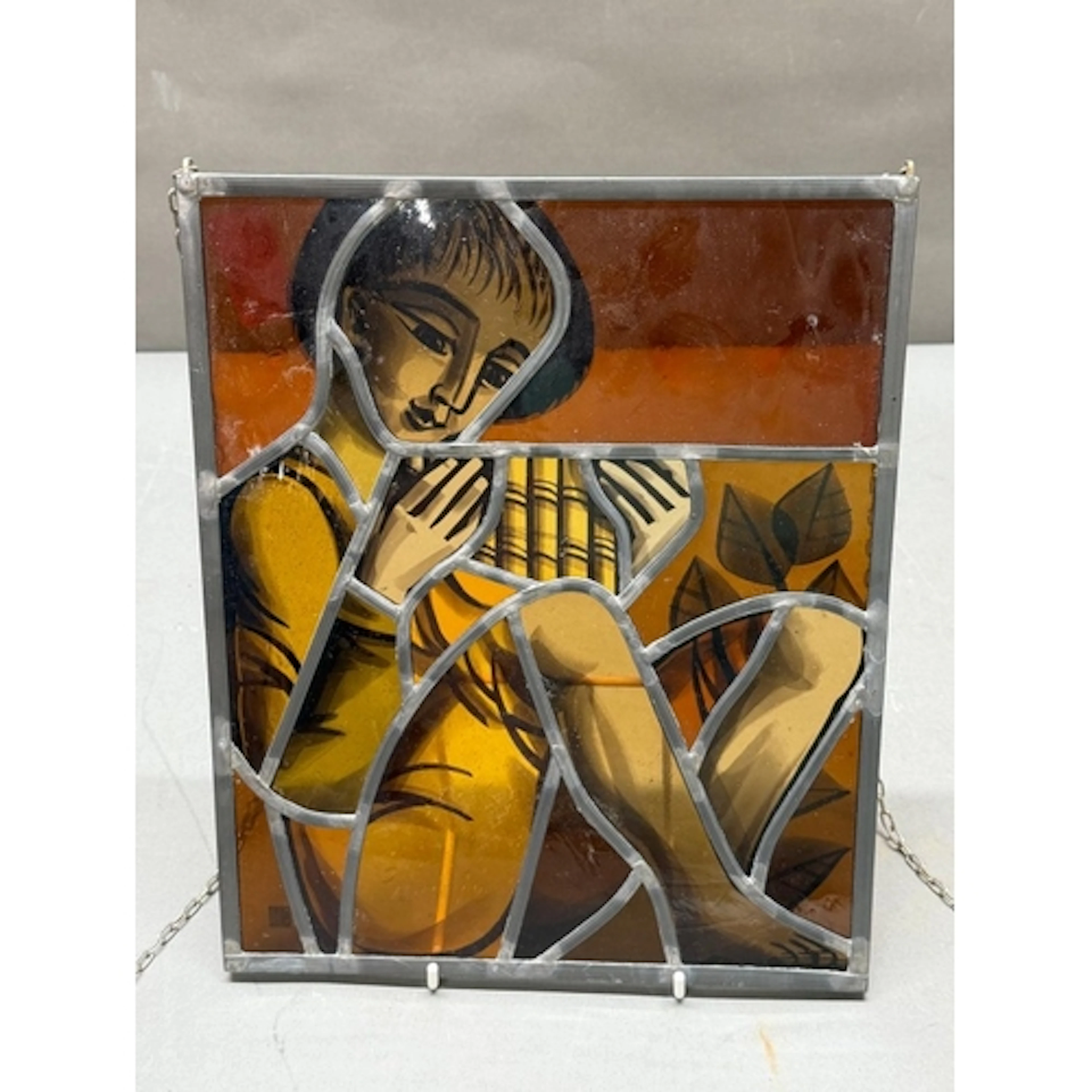 A stained glass figure of a stylised woman in orange an ambe...