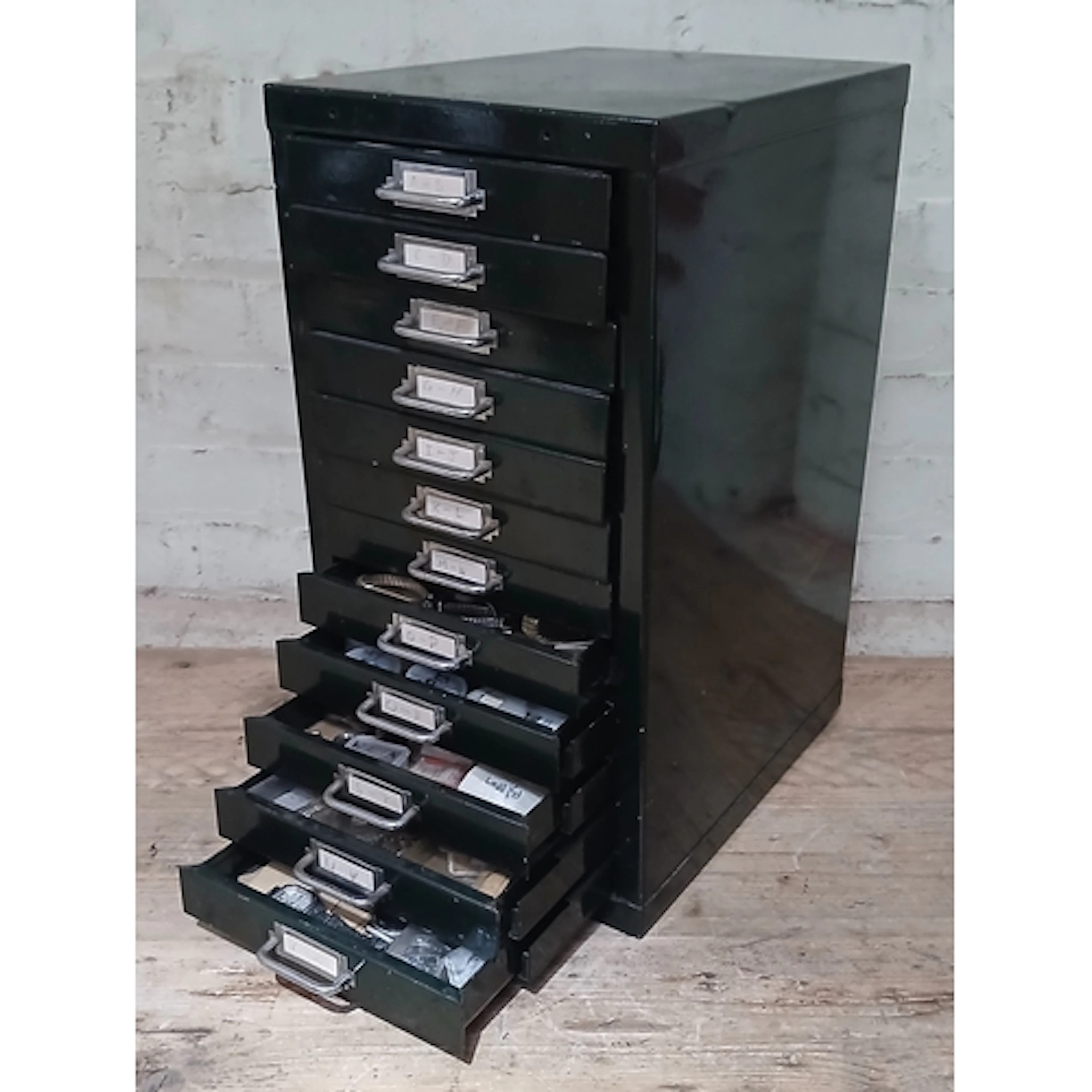 A green metal twelve drawer filing cabinet containing assort...