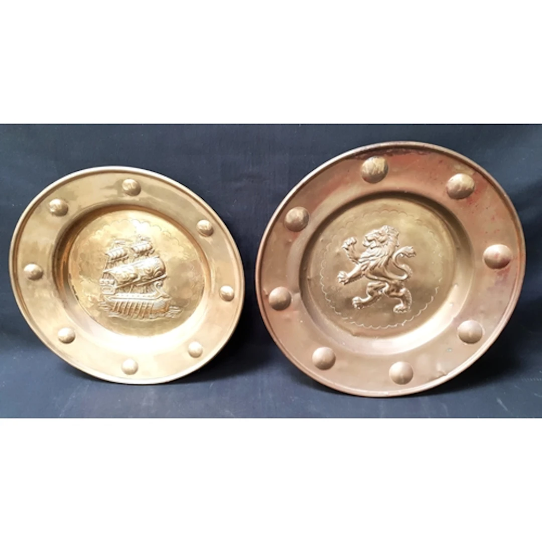 TWO RELIEF DECORATED BRASS WALL CHARGERS one with central li...