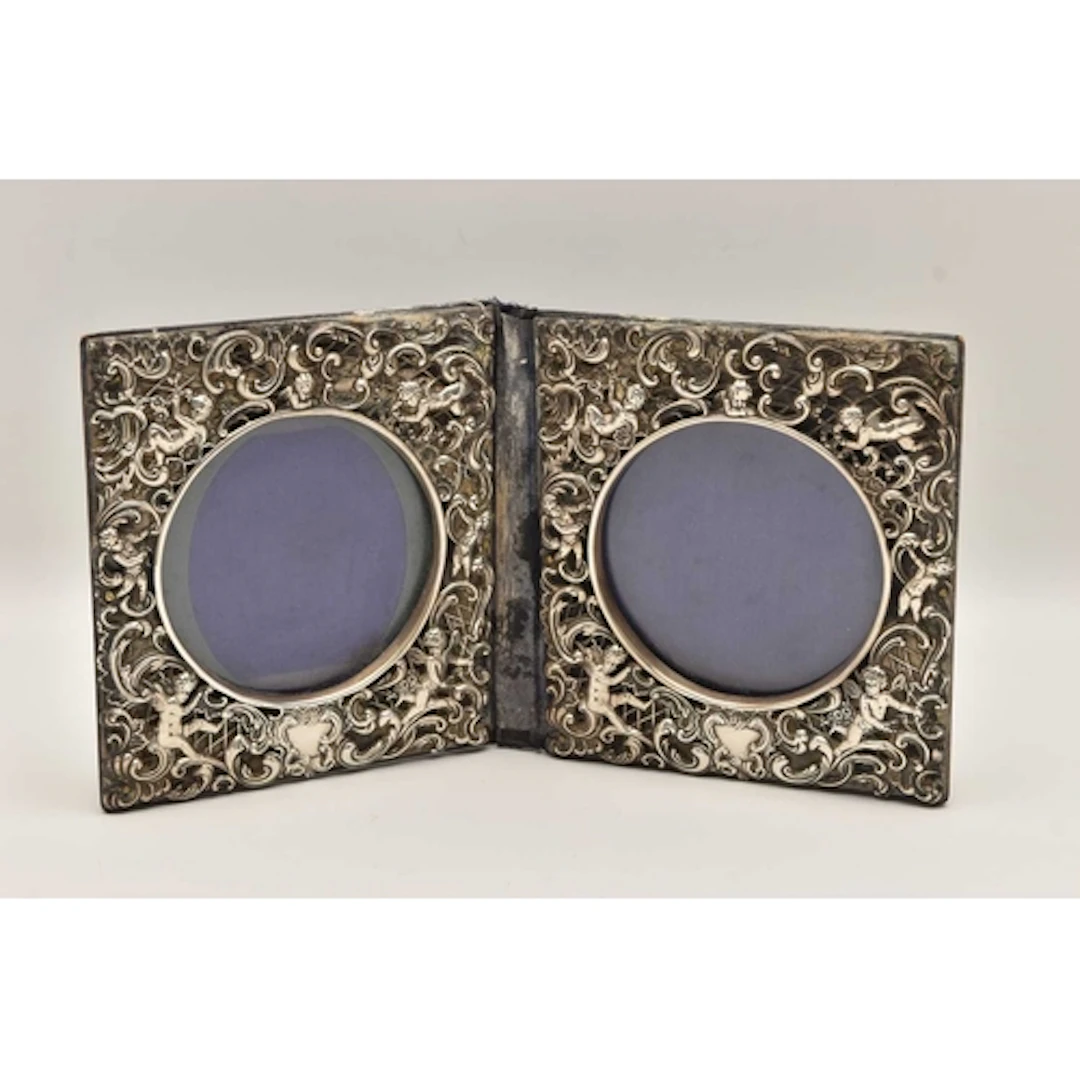 A DOUBLE PHOTO FRAME, white metal depicting cherubs with scr...