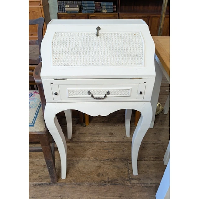 A small white painted bureau with cane panels standing on ca...