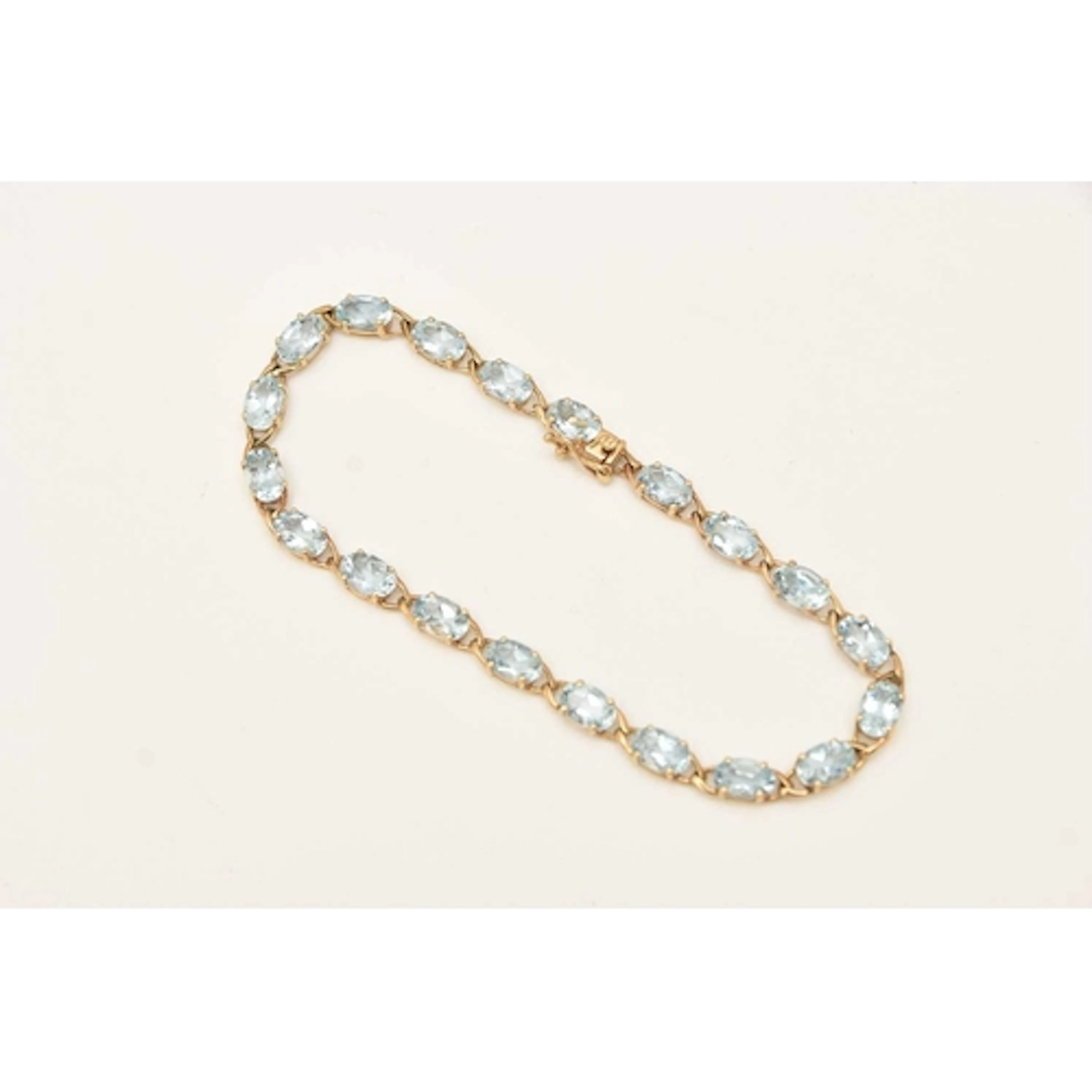 A 9CT YELLOW GOLD GEM SET LINE BRACELET, oval cut light blue...
