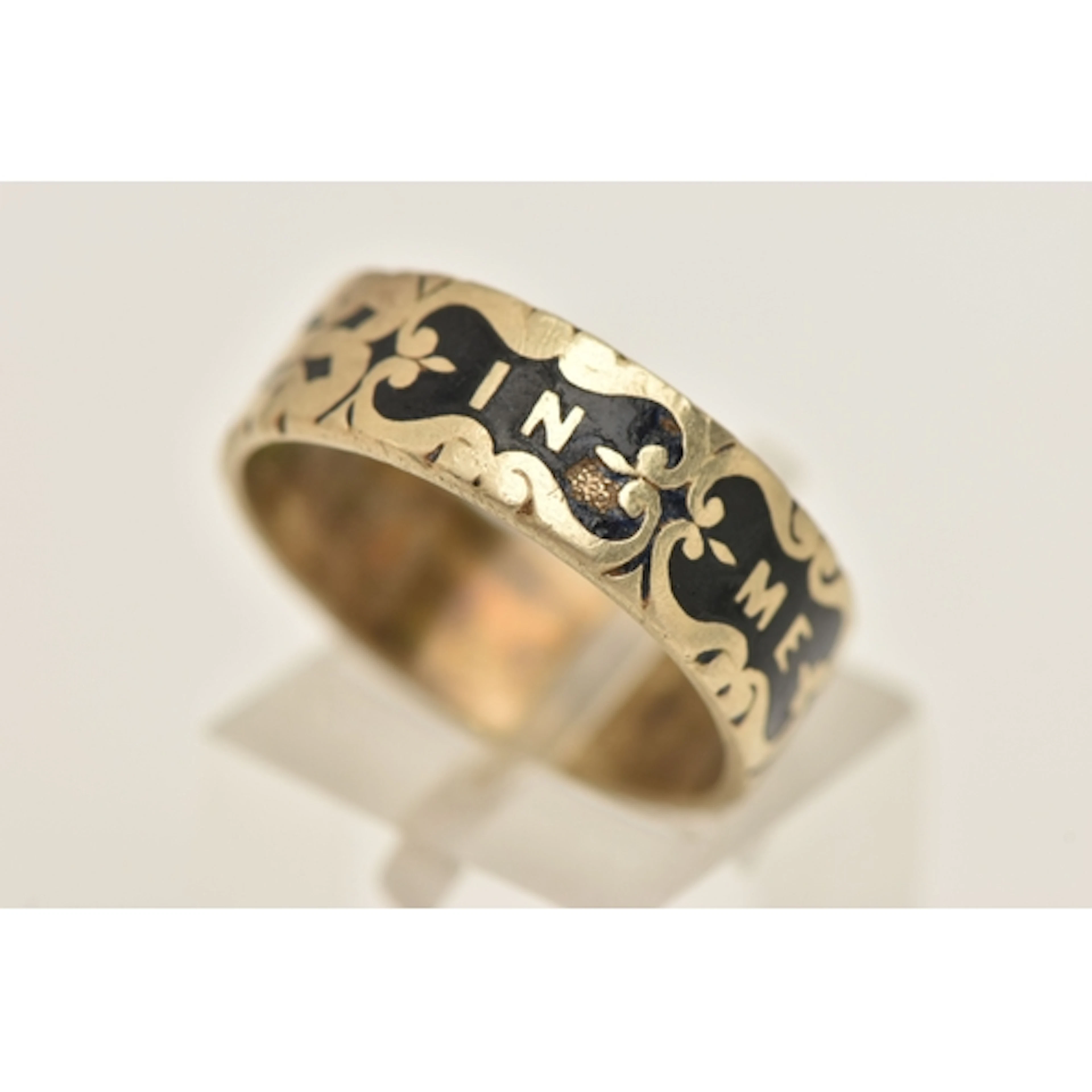 A YELLOW METAL AND BLACK ENAMEL 'IN MEMORY OF' WIDE BAND RIN...