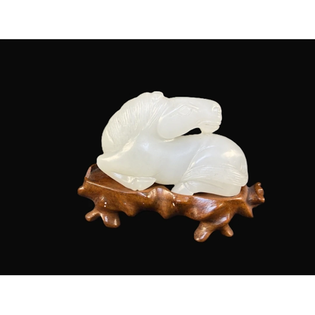 A Chinese pale jade colour carved reclining horse, on hardwo...