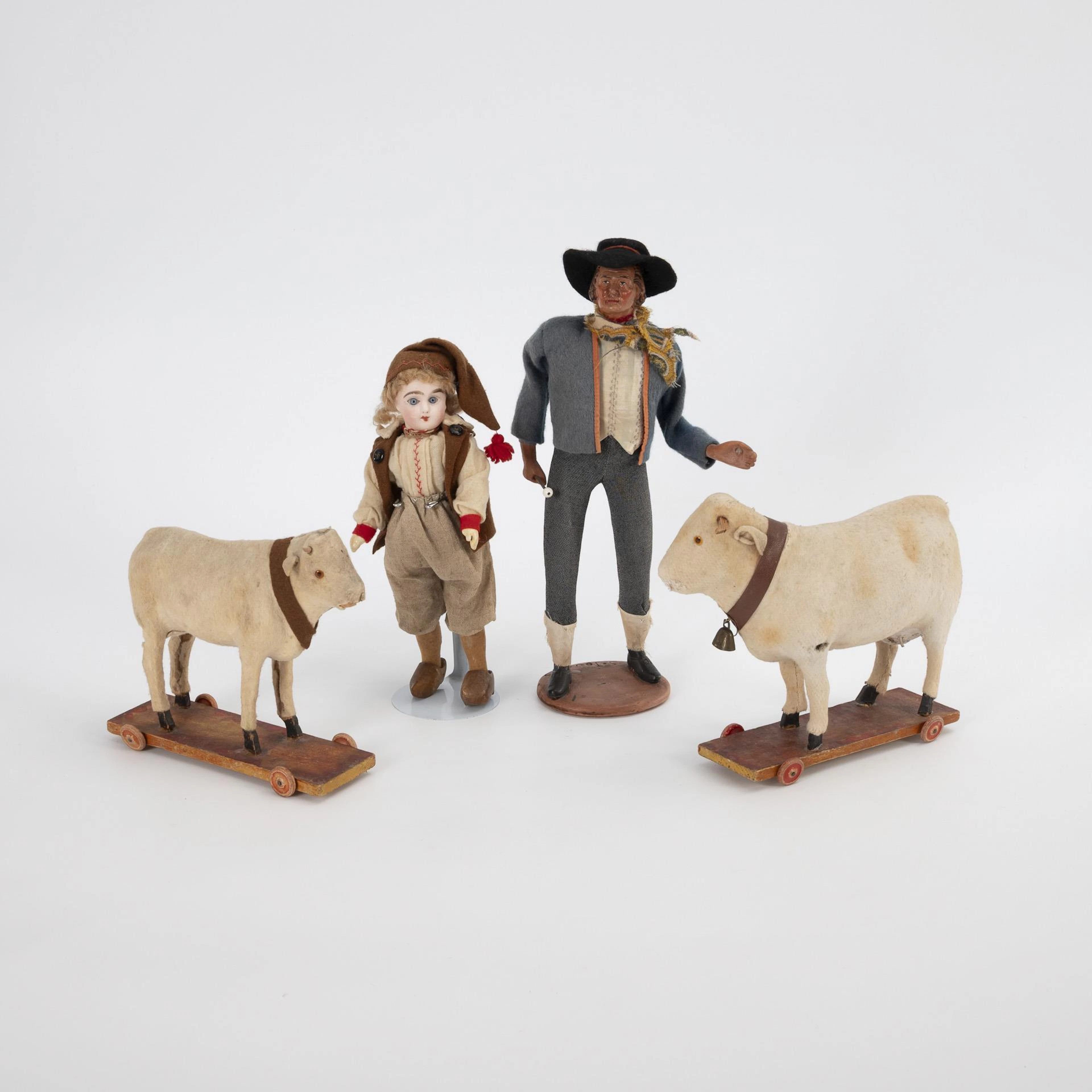 Porcelain head doll, terracotta figure and 2 cows on wheeled plate.