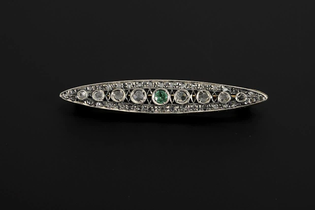 Art Deco-style brooch with diamond chips and a green gemstone, likely