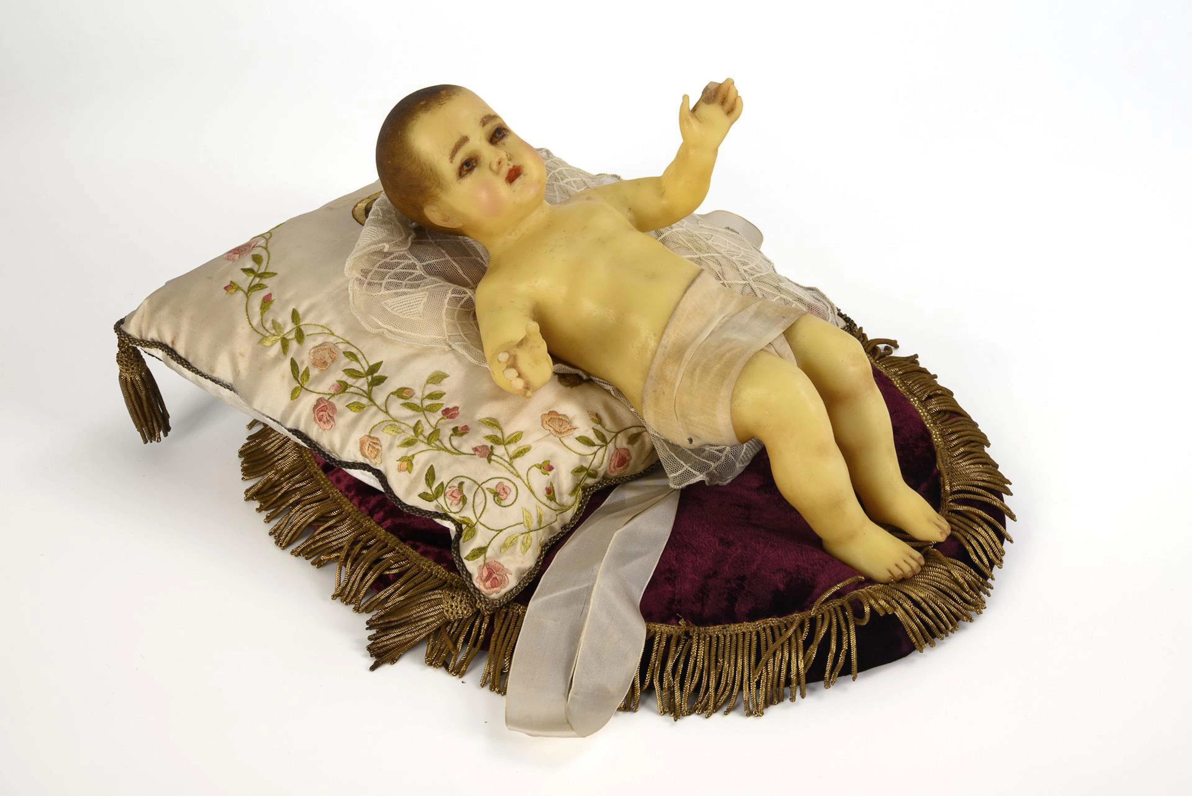 Wax baby Jesus, on 2 cushions.