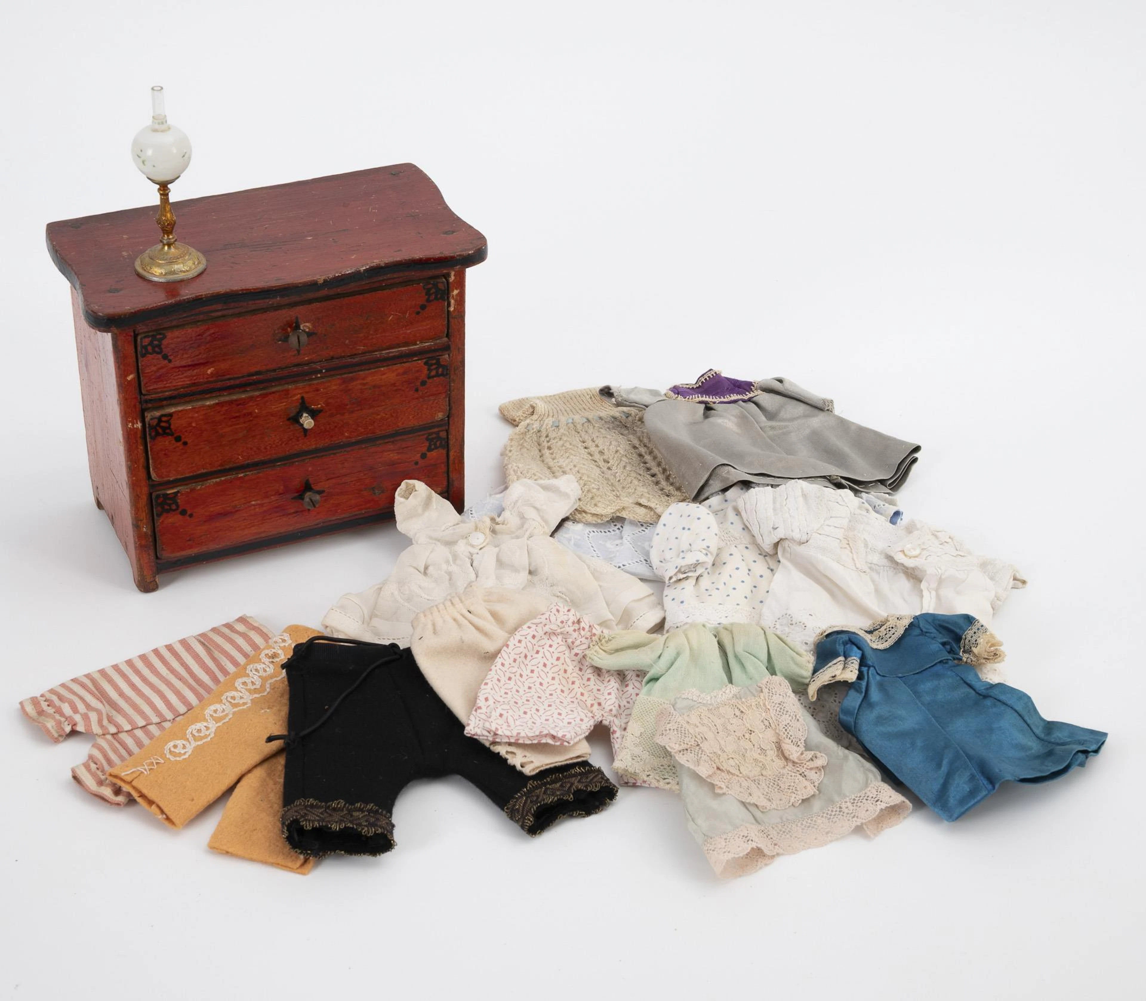 Small chest of drawers, kerosene lamp and bundle of clothes for small dolls.