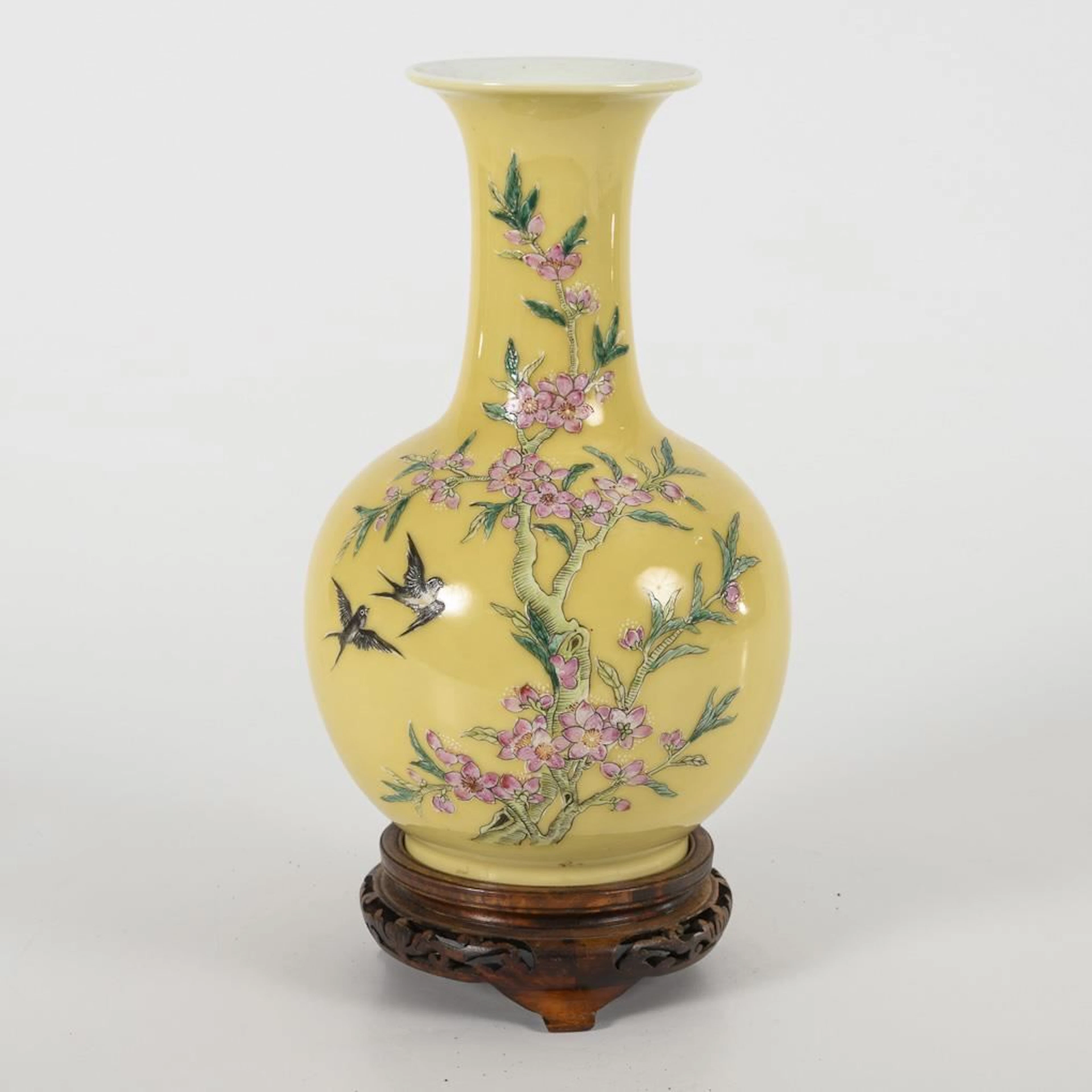 Yellow vase with pink flowers, on a pedestal.