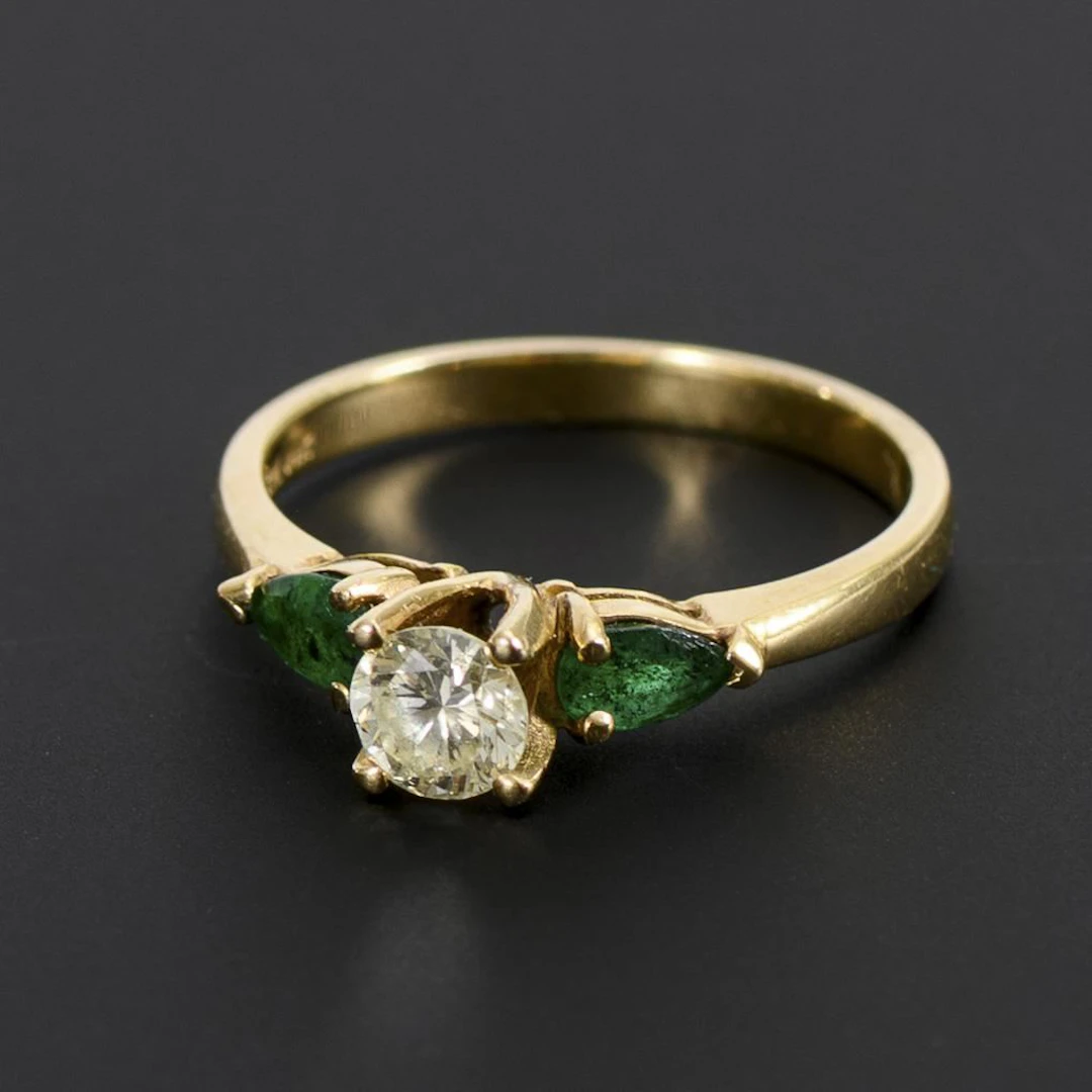 Ring with a brilliant-cut diamond and green gemstones, likely emeralds.