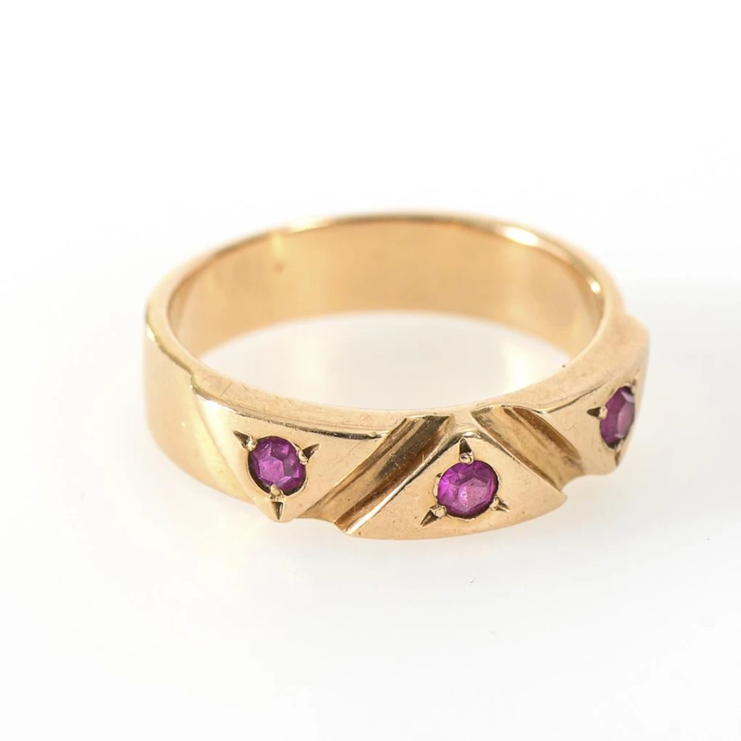 Band ring with a raised decorative pattern and 3 red gemstones.