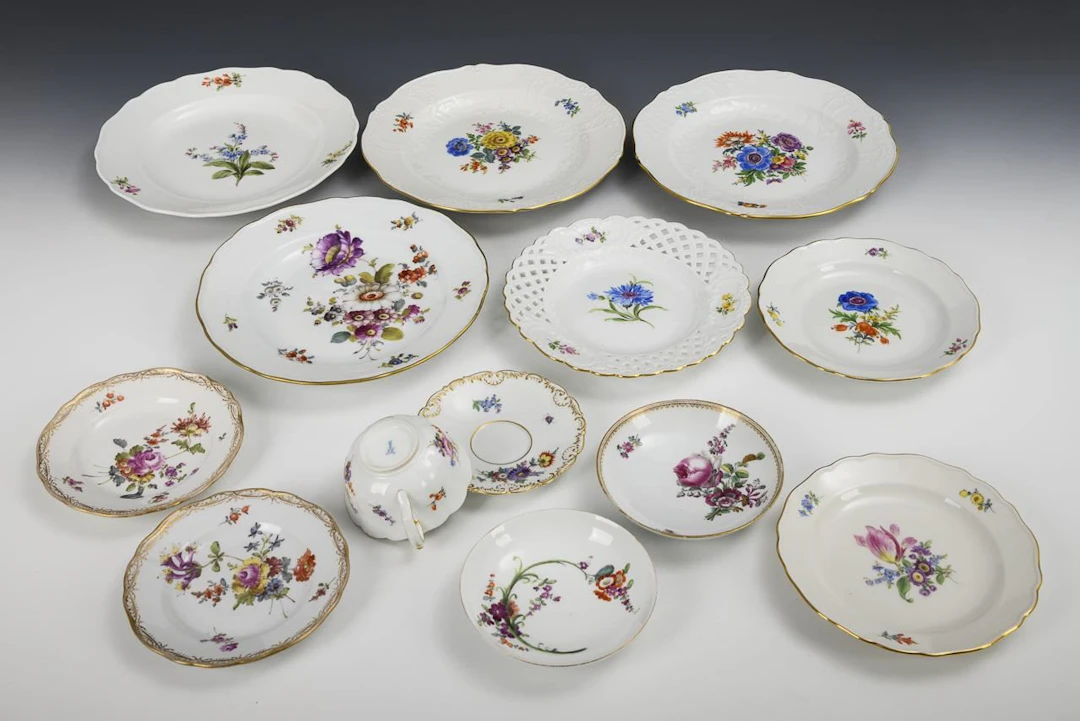 12 plates and 1 cup with floral designs. Meissen.