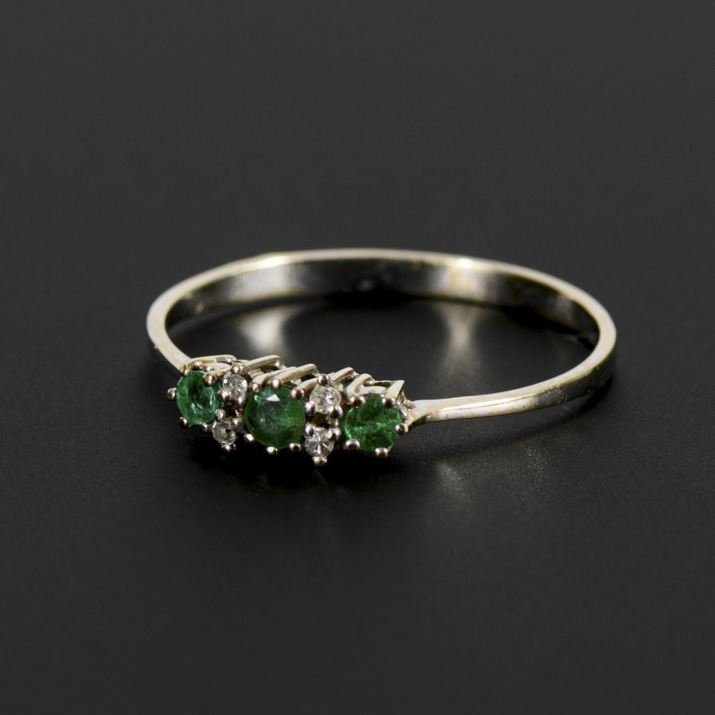 Delicate ring with green colored stones, probably emeralds, and diamonds.