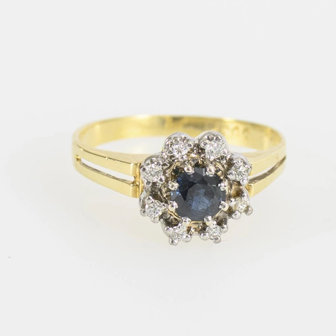 Daisy ring with a blue gemstone, likely a sapphire, and brilliant-cut diamonds.