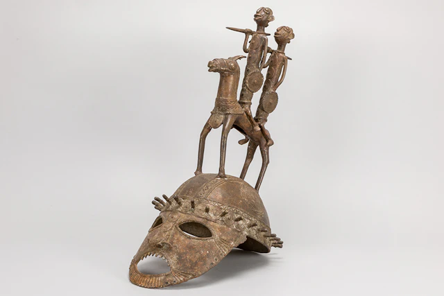 Afrikaanse sculptuur in brons met helmvorm bekroond met figuren -