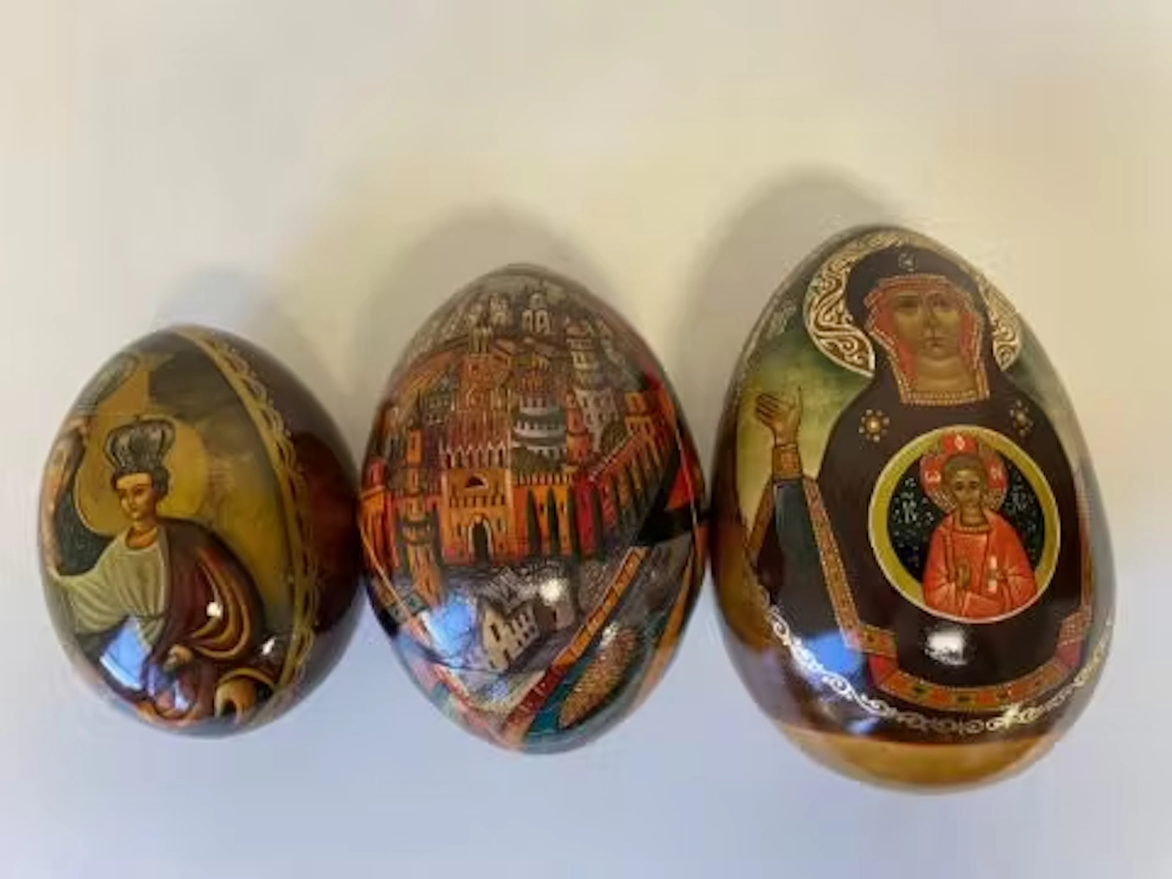 Three Russian lacquered eggs decorated with icons and other religious