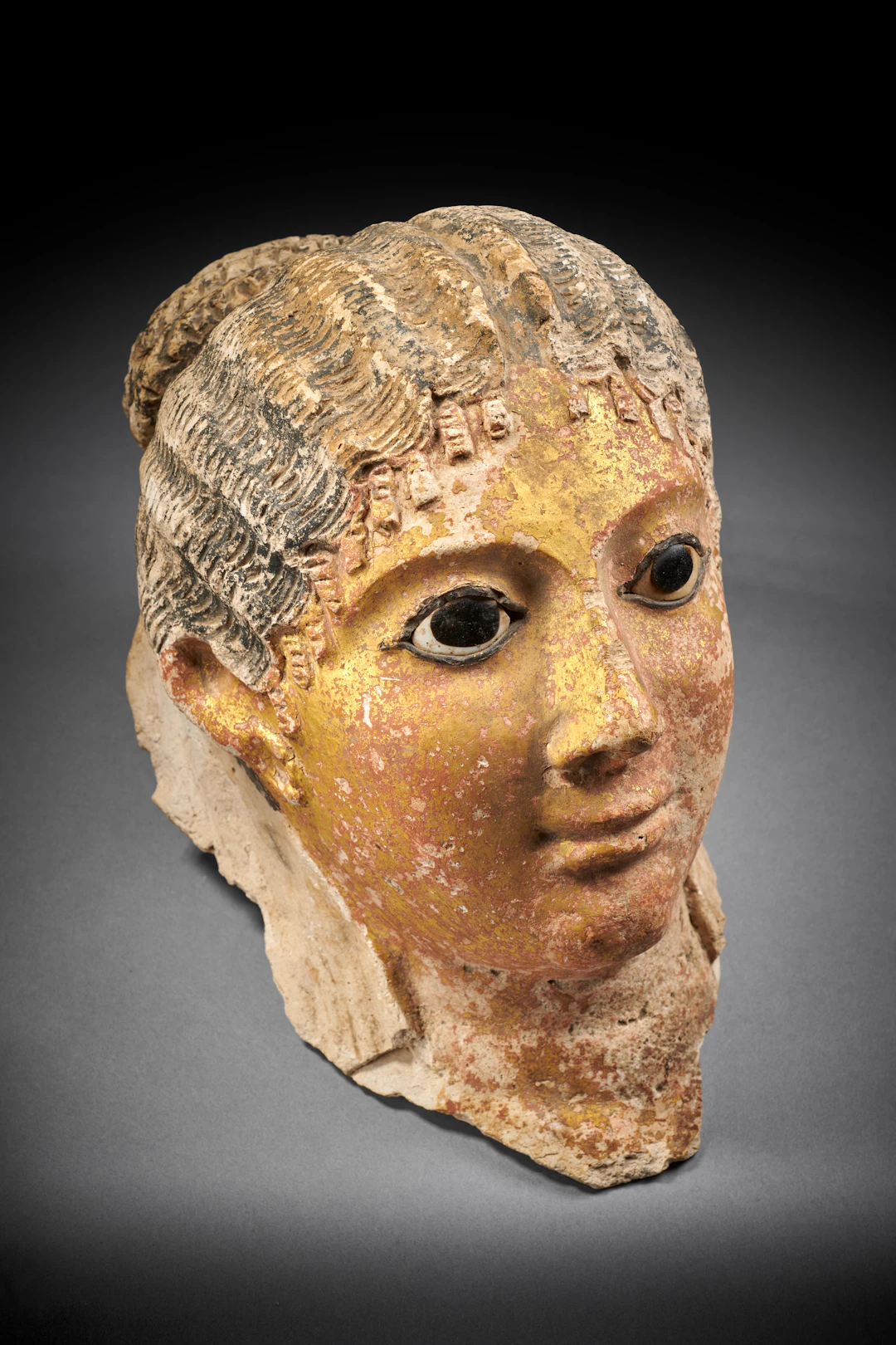An Egyptian painted and gilded stucco mummy mask of a woman with inlaid