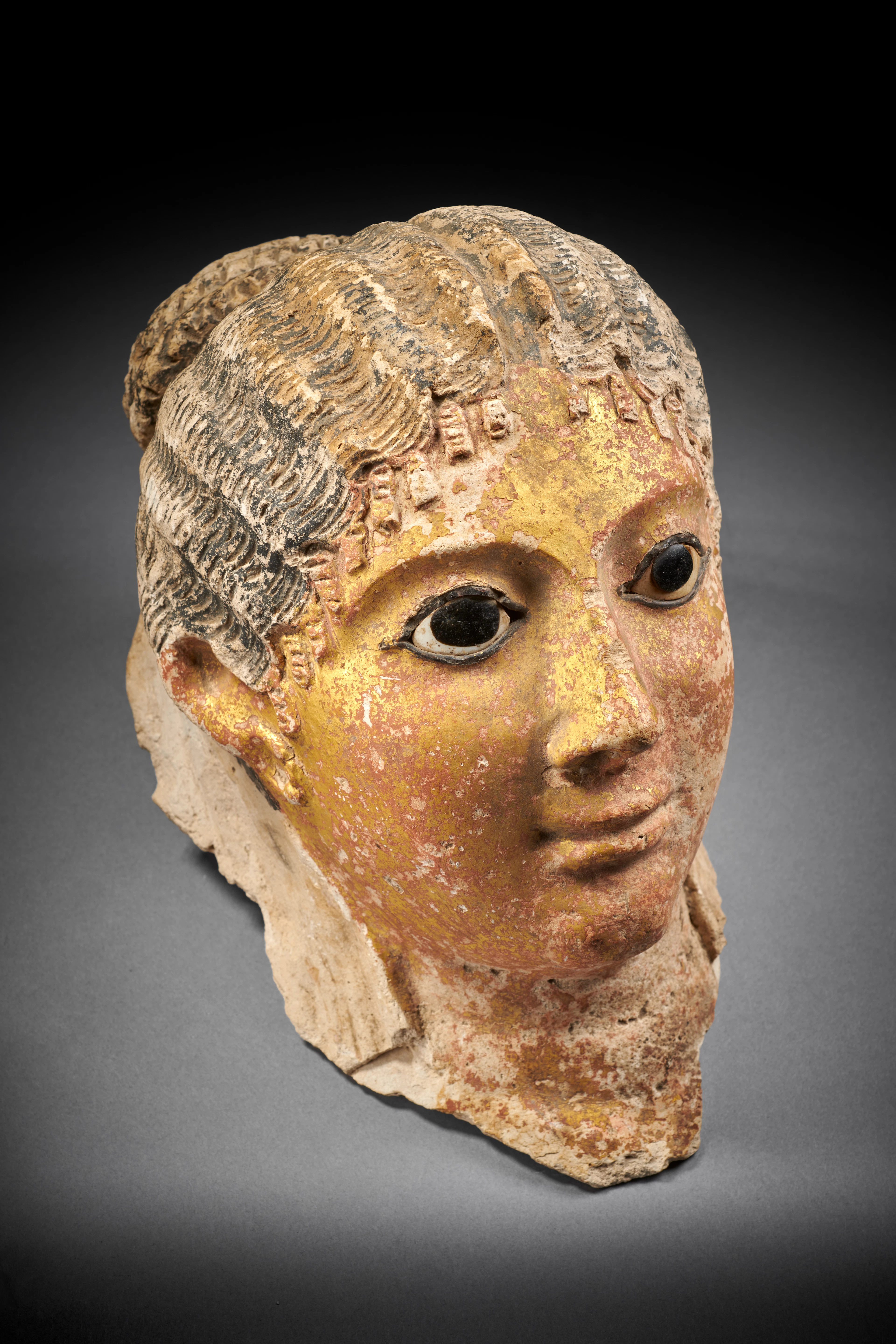 An Egyptian painted and gilded stucco mummy mask of a woman with inlaid