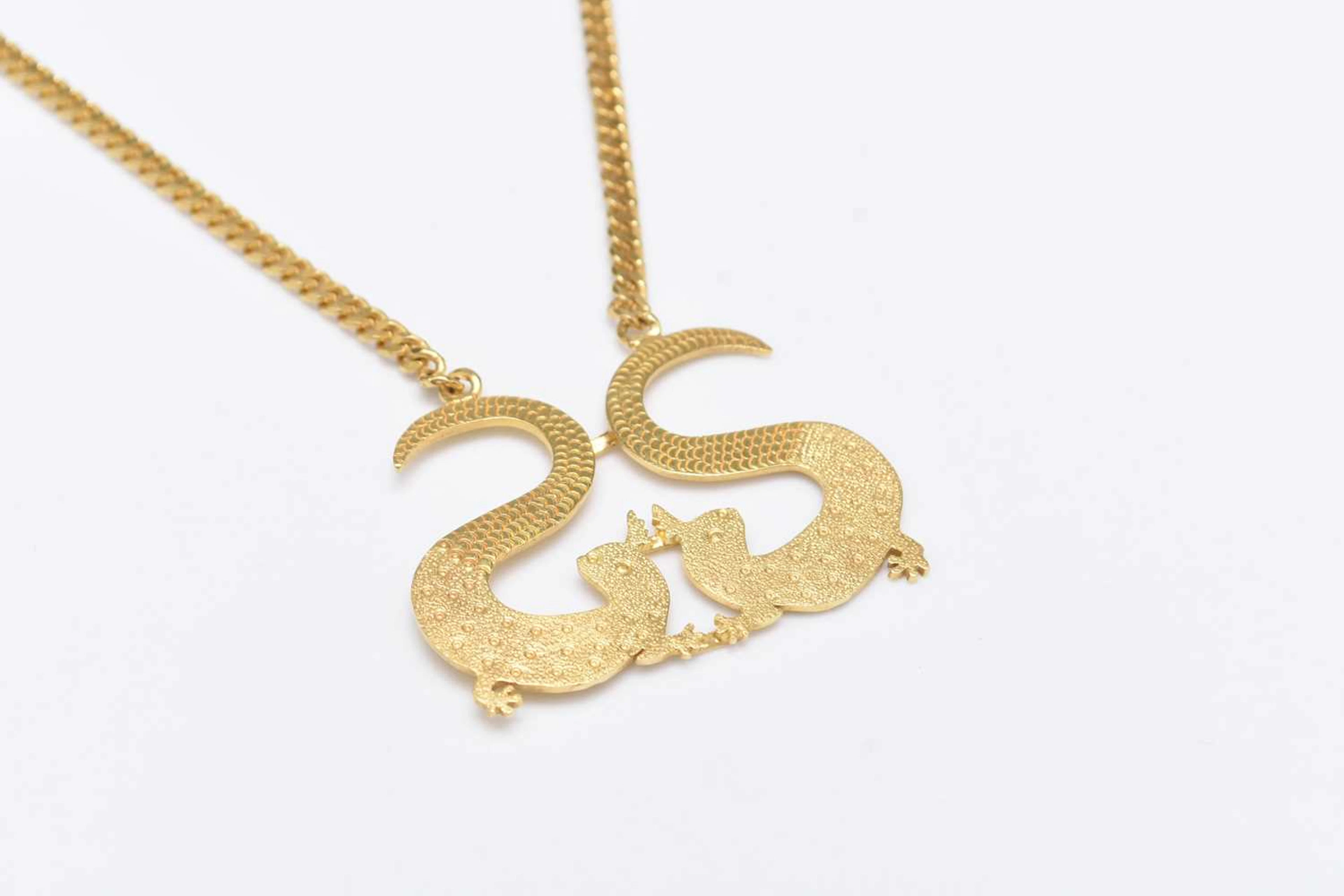 A yellow metal pendant designed as two stylised Geckos